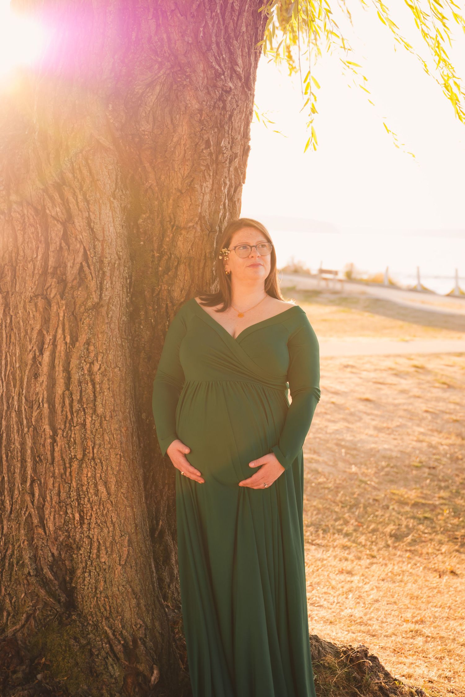 A person in a flowing emerald green dress stands in golden sunlight beneath a large tree in an autumn setting.