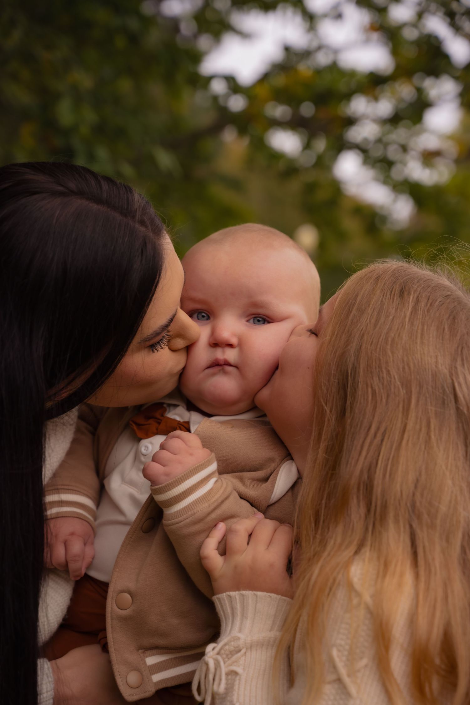 A sweet sequence of family members giving kisses to a baby wearing a beige sweater outdoors.