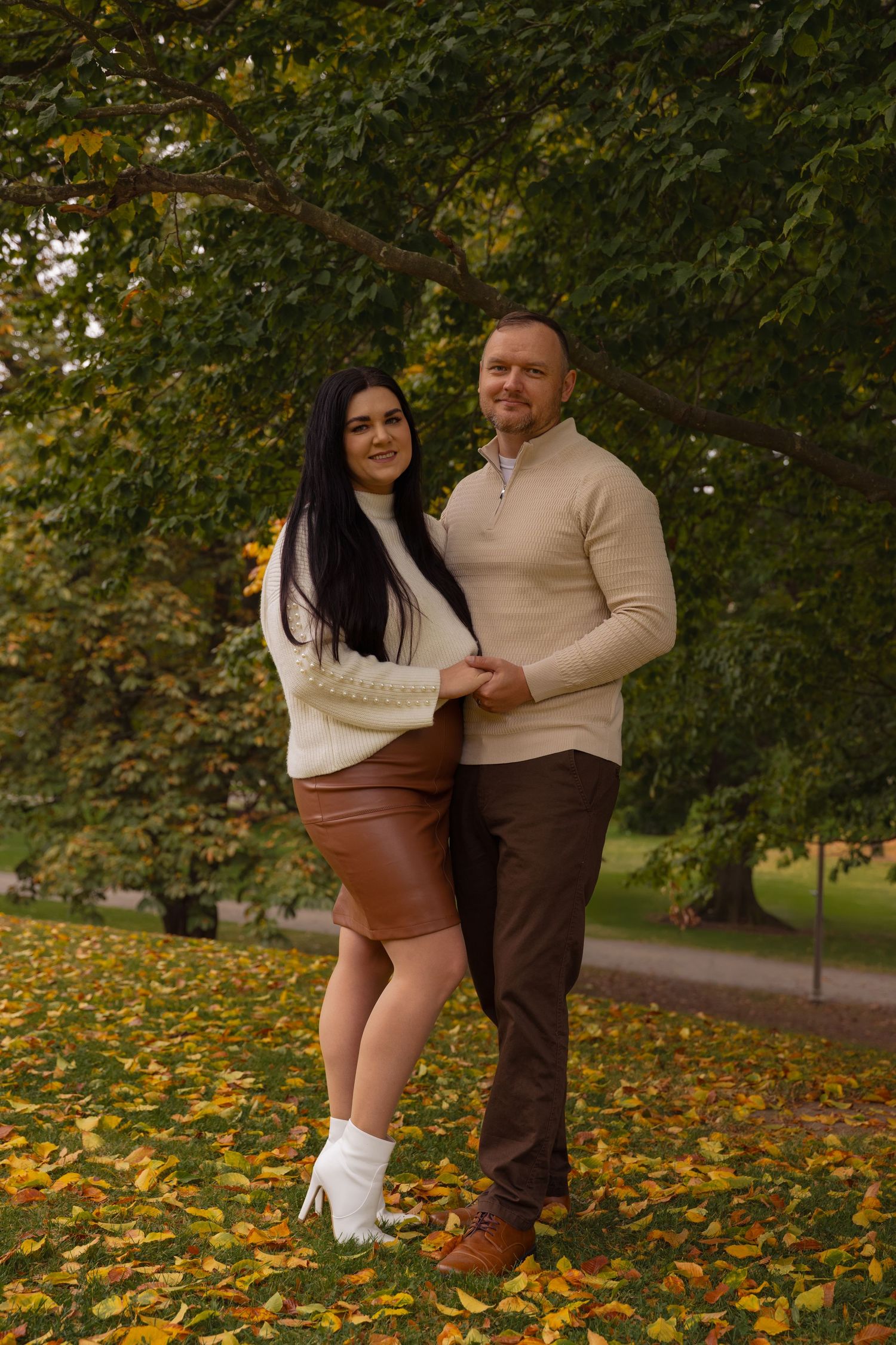 A couple embraces in a park during autumn with fallen yellow leaves scattered on the ground.