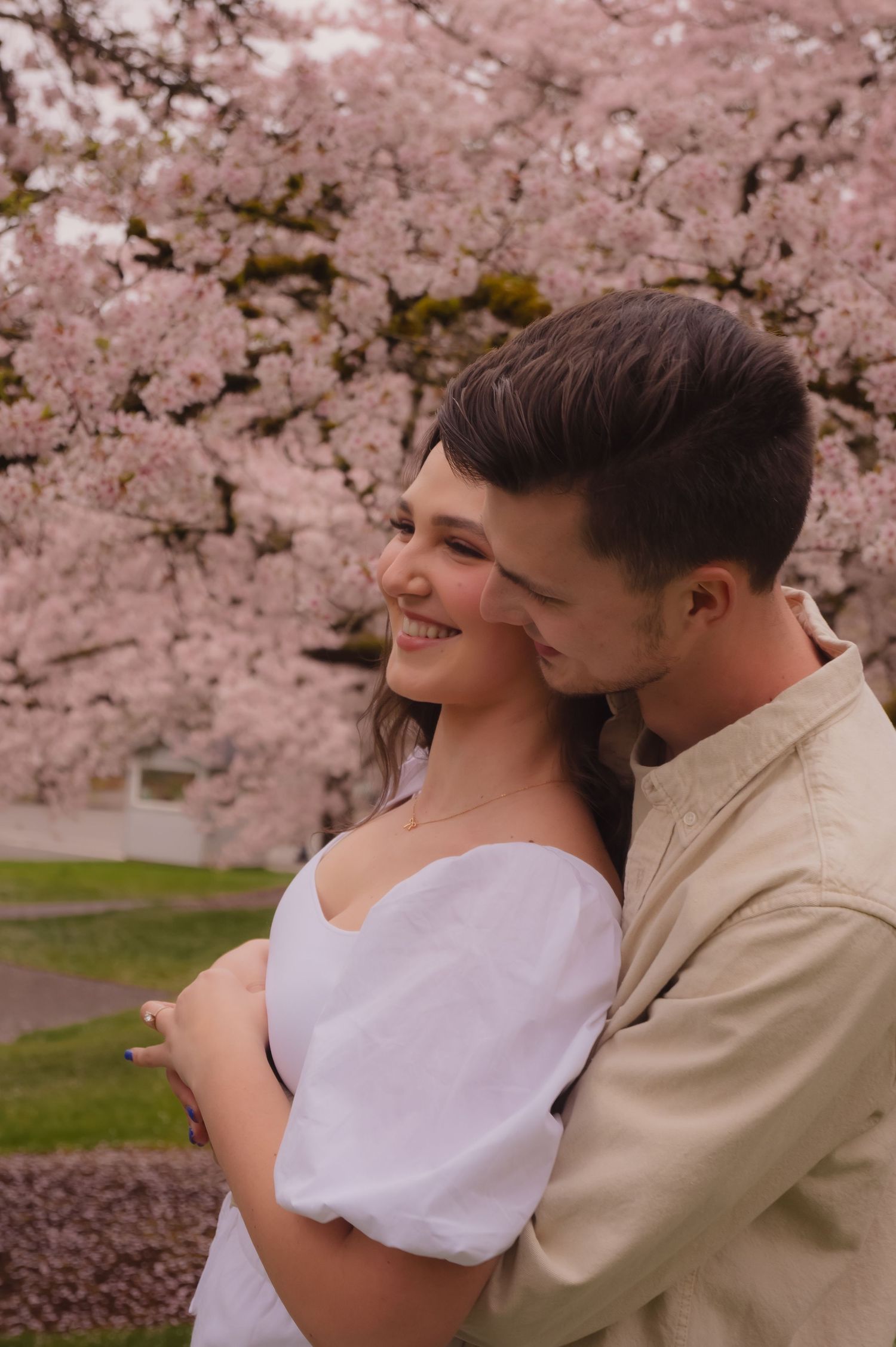 A couple embraces under blooming pink cherry blossom trees during springtime.