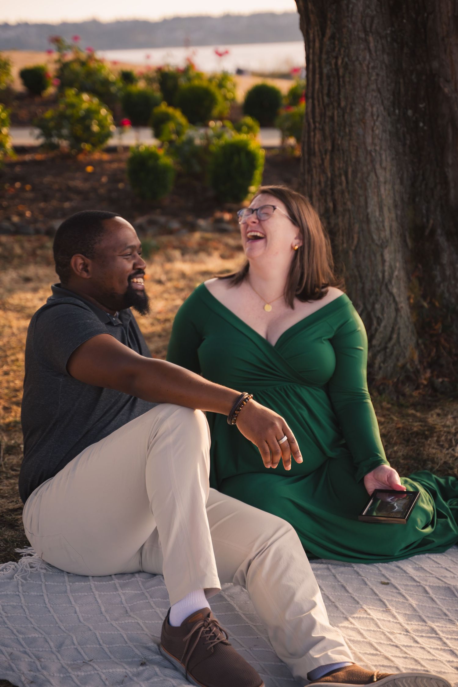 Two people sitting together on a blanket outdoors sharing a joyful moment at sunset.