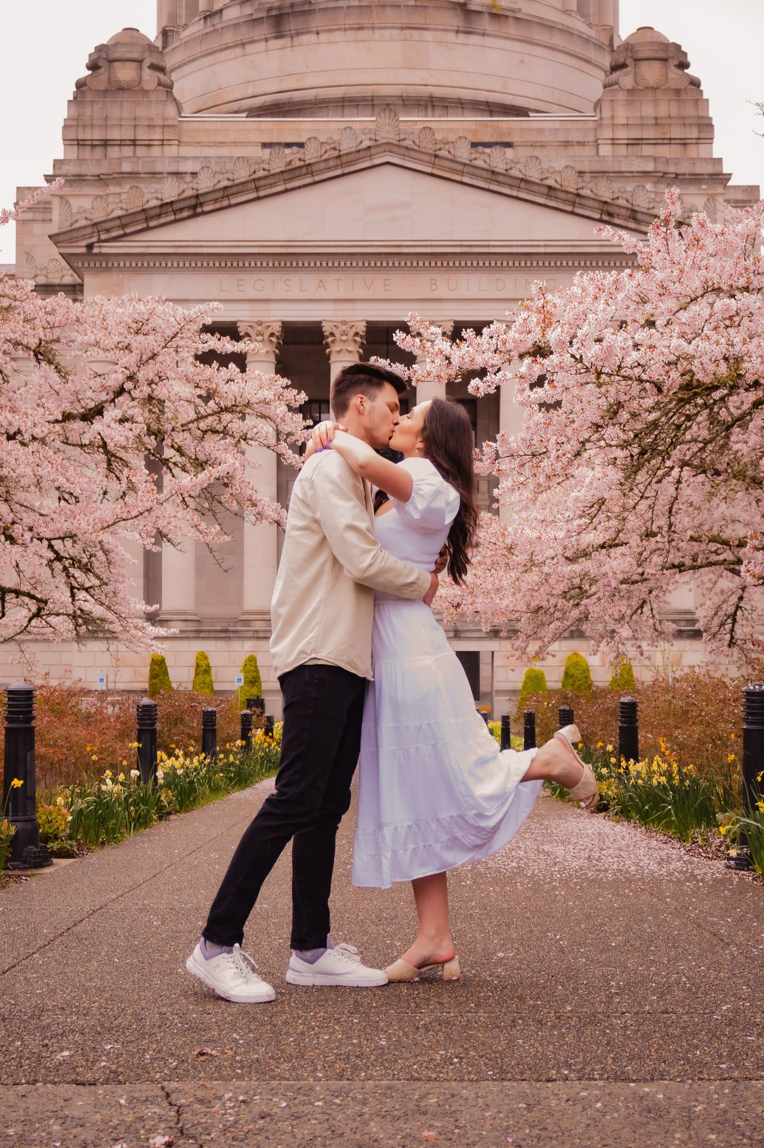 A romantic couple dances together surrounded by blooming cherry blossoms and classical architecture.