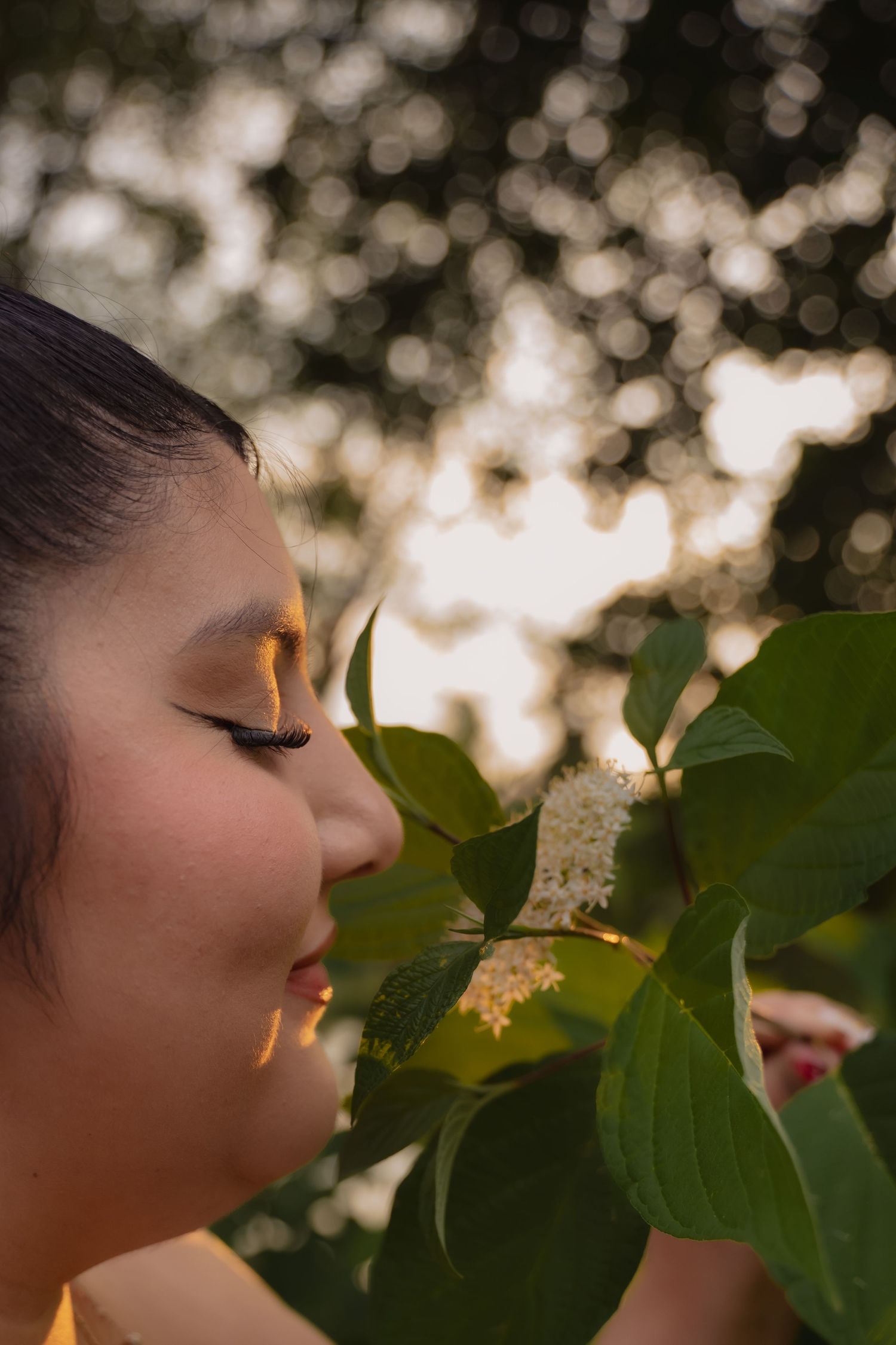A peaceful moment in nature as someone smells white flowers on a tree branch with soft bokeh lighting in the background.