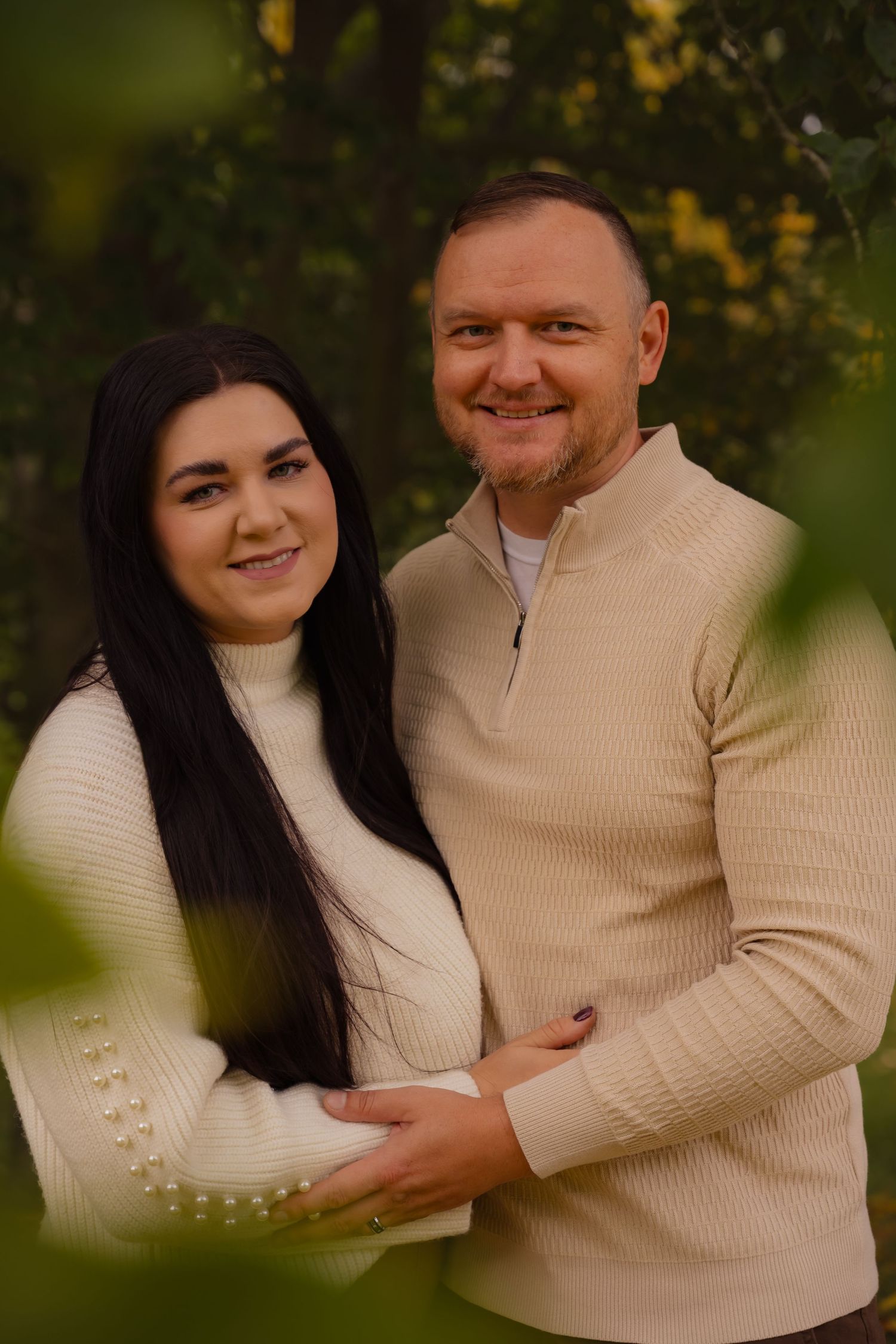 A couple in matching cream sweaters embrace outdoors in a romantic autumn photoshoot series.
