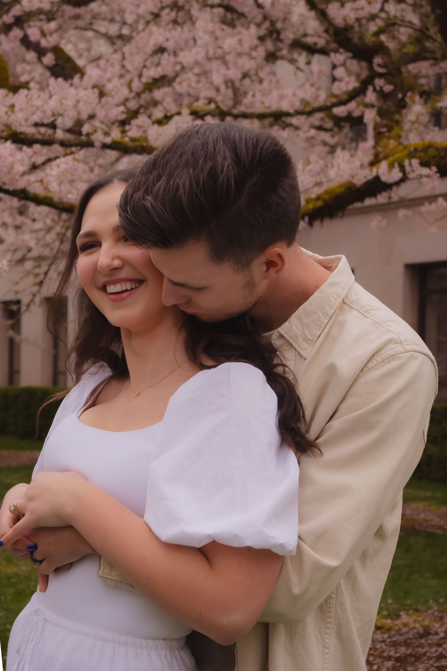A romantic couple embraces under blooming cherry blossom trees on a spring day.