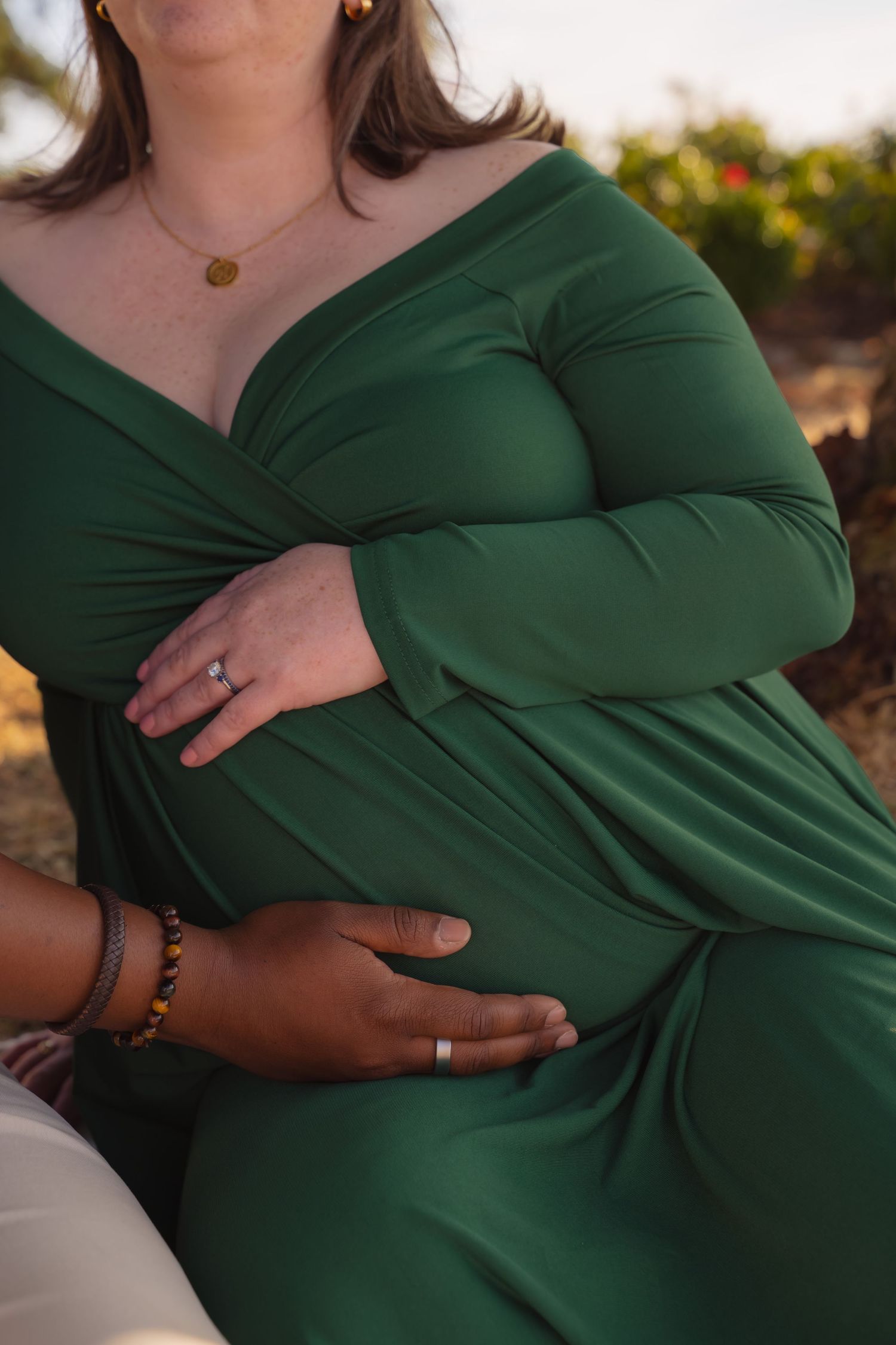 Close-up shots of a person wearing an emerald green wrap dress in an outdoor maternity photoshoot at sunset.