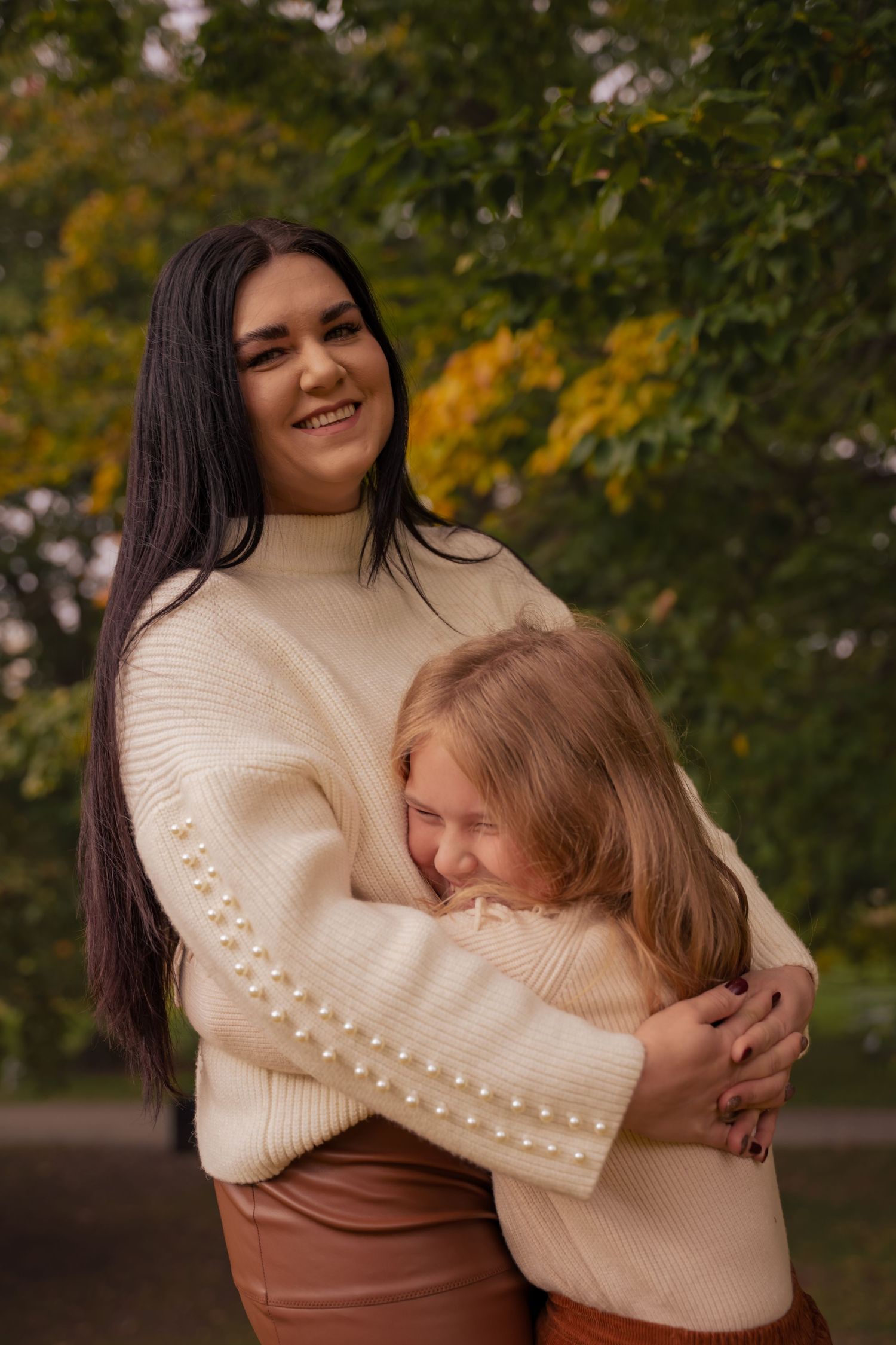 A warm embrace between two people wearing cream sweaters against an autumn background with blurred trees.