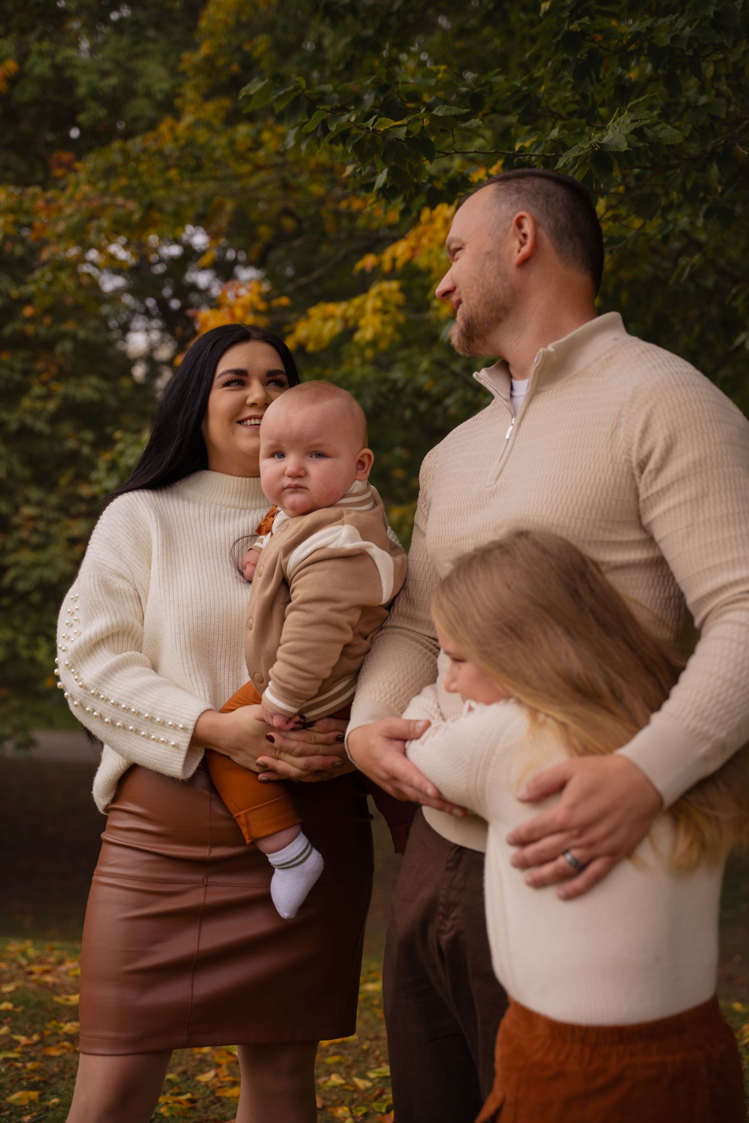 Family wearing cream and brown coordinated outfits poses together during autumn outdoor photoshoot.