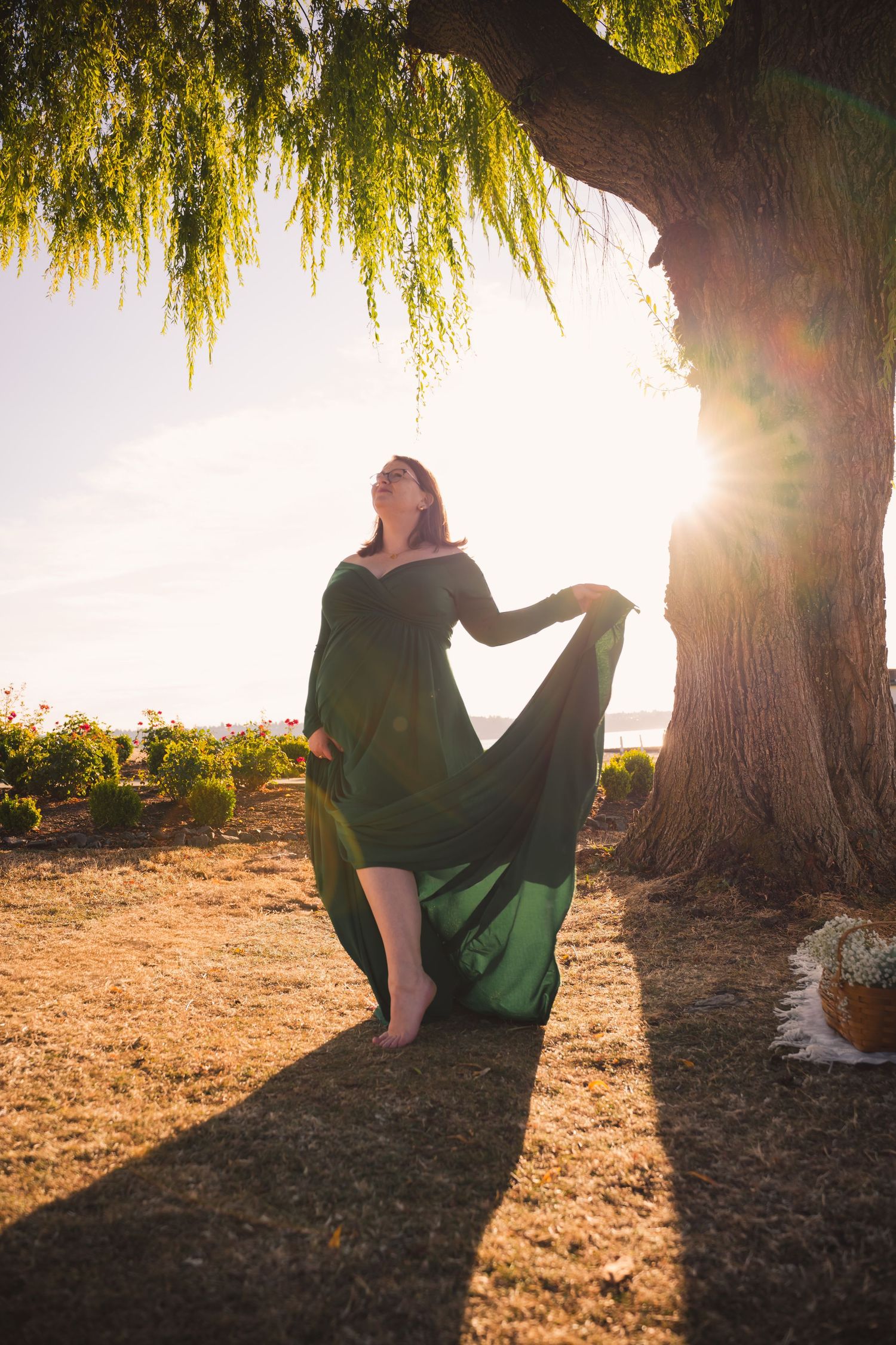 Silhouetted figure sits under willow tree branches at sunset creating a dreamy golden backlit scene.