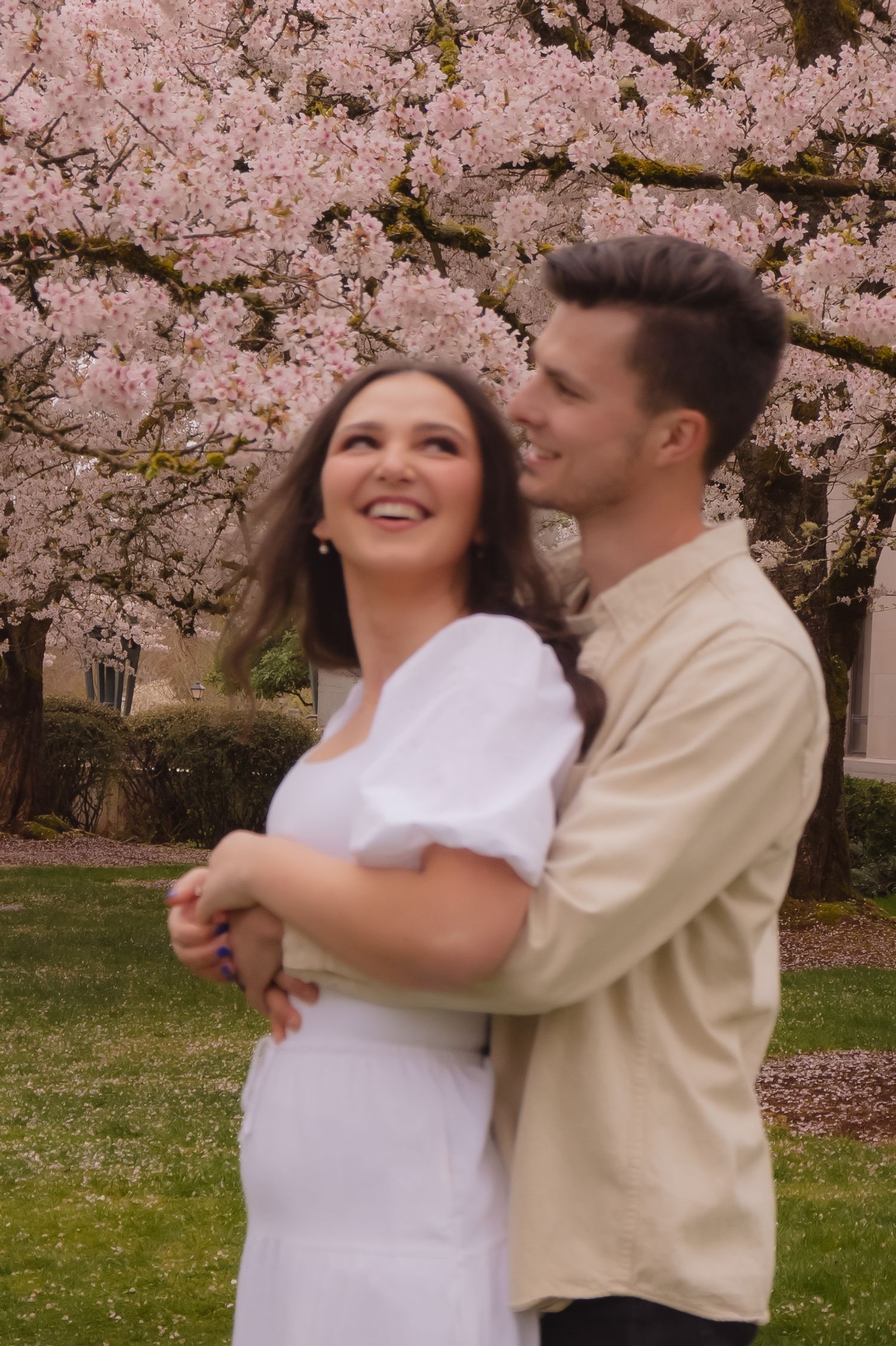 A couple shares a joyful moment under blooming cherry blossom trees in spring.