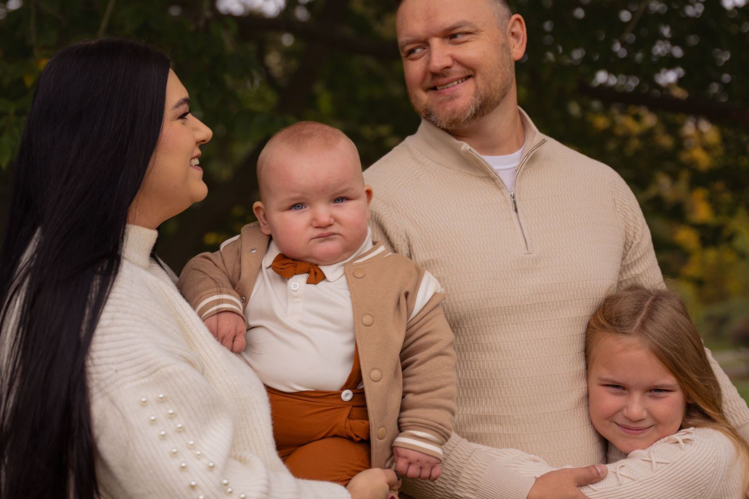 Family wearing coordinated beige and white outfits poses together during an outdoor autumn photoshoot.