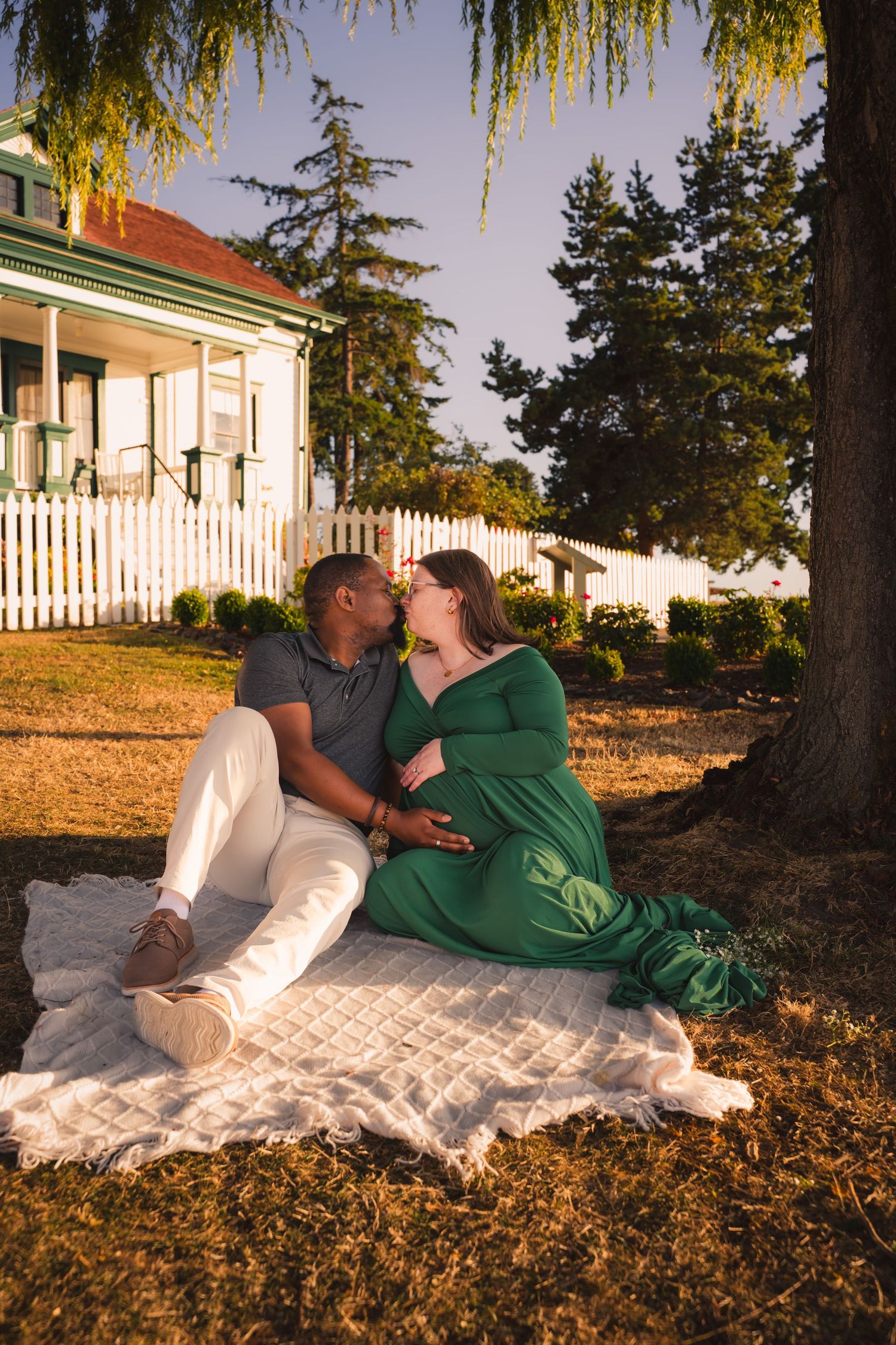 Couple relaxing together on a white blanket under a willow tree during golden hour sunset.