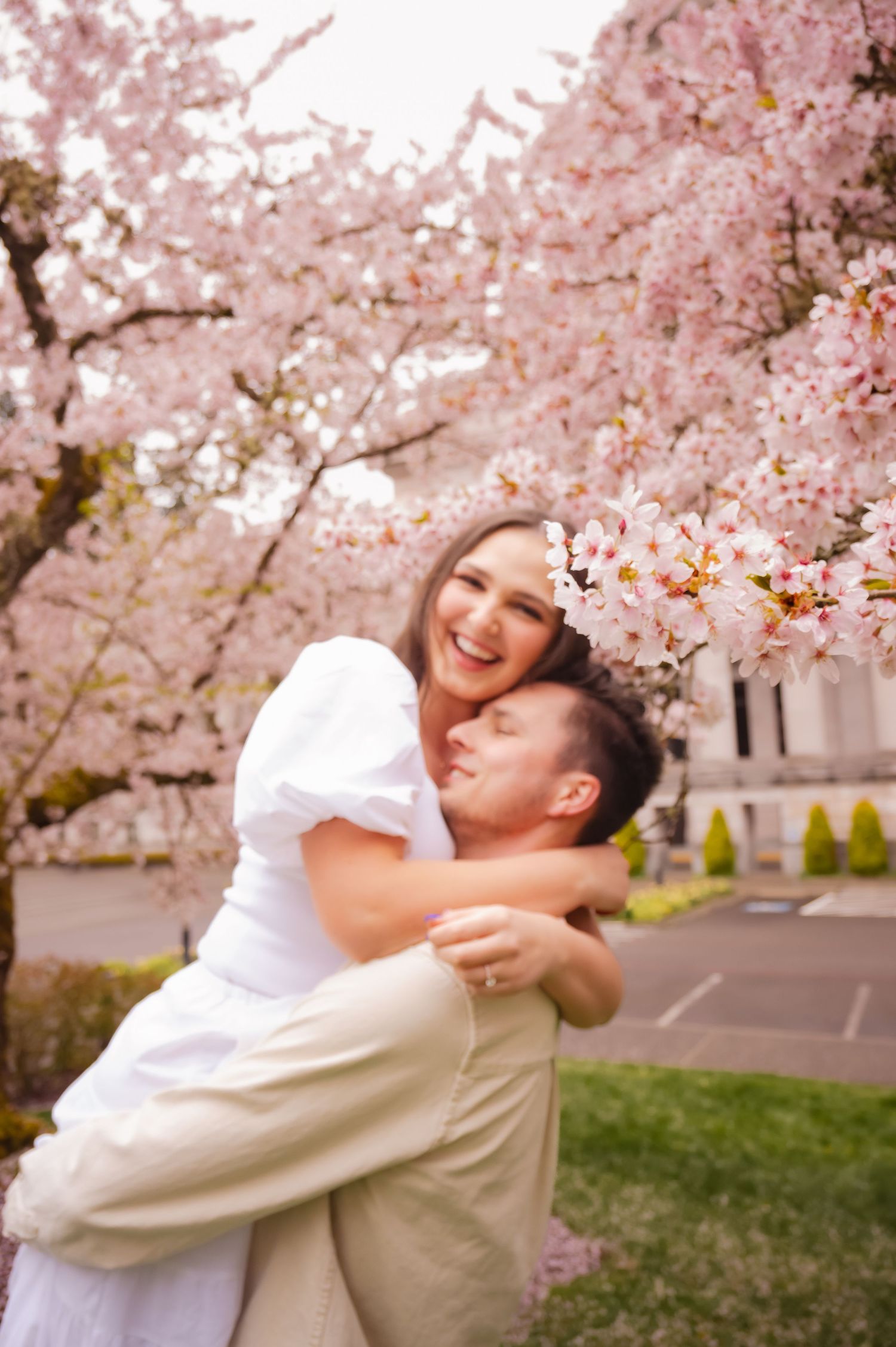 A couple embraces under blooming cherry blossom trees on a spring day.