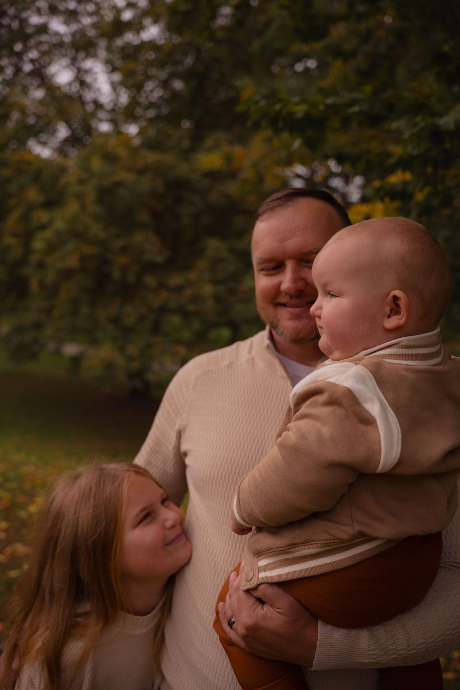 A tender family moment captured outdoors with a baby in a brown sweater during autumn.