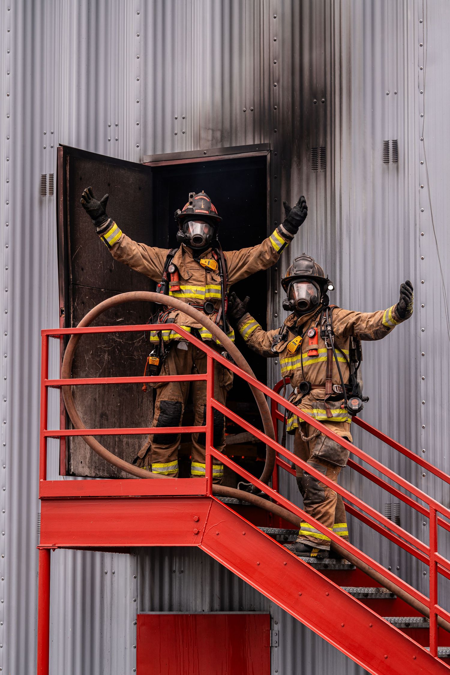 Firefighters in protective gear practice rescue operations on red metal stairs during a training exercise.