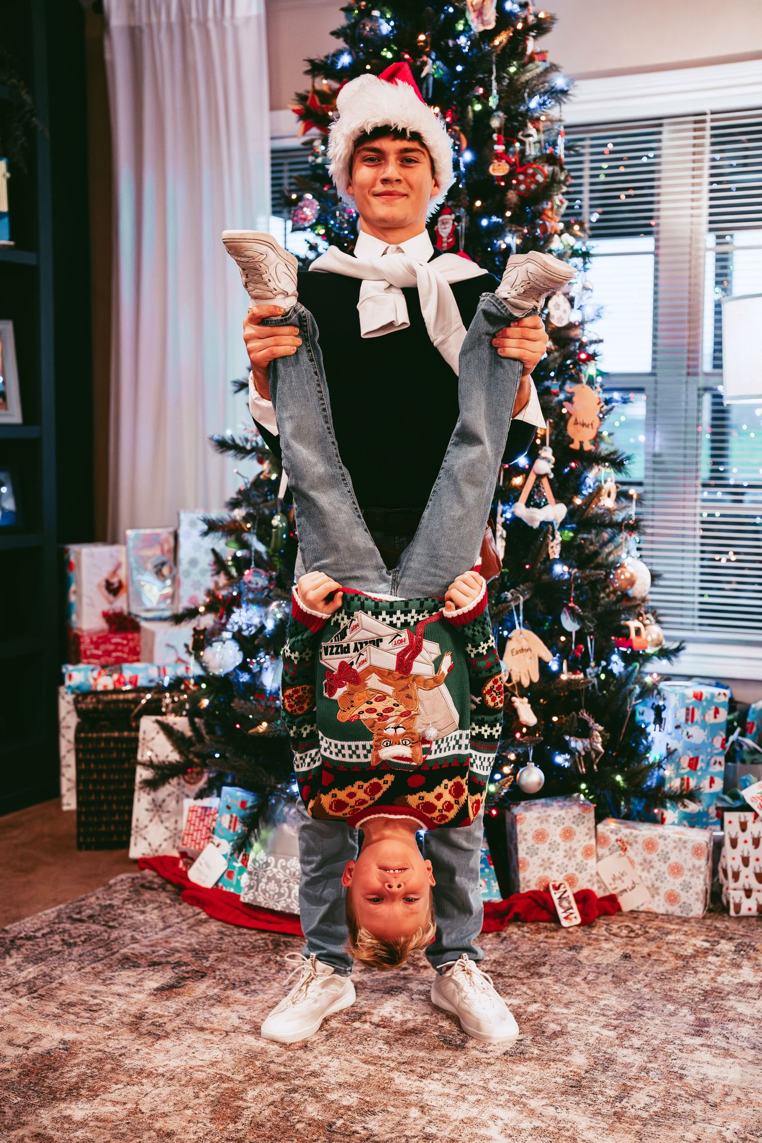 A playful Christmas scene with someone doing a handstand among wrapped presents and a decorated tree.