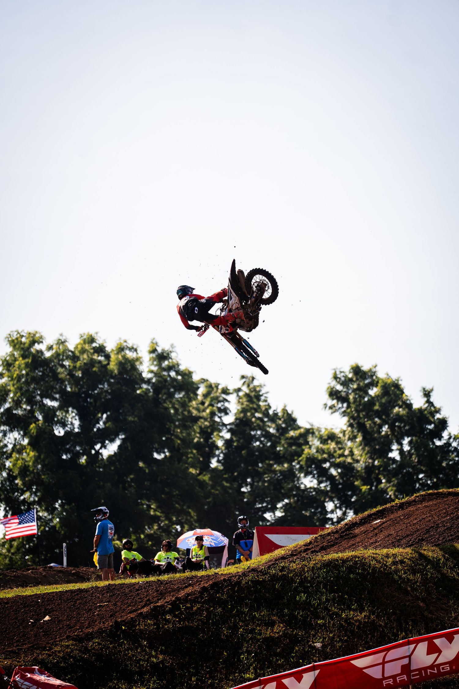 Silhouetted motocross rider performing backflip trick against white sky.