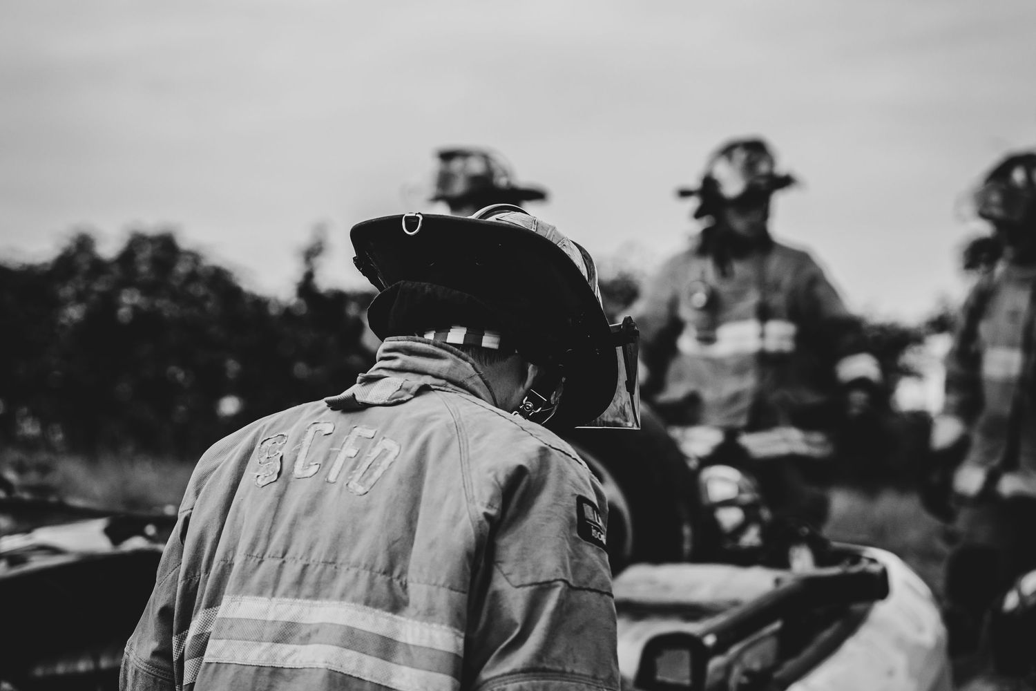 Group of firefighters in turnout gear standing together outdoors.