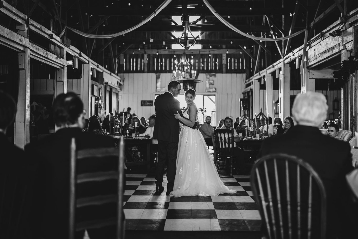 Black and white wide shot of indoor wedding reception venue with dramatic lighting.