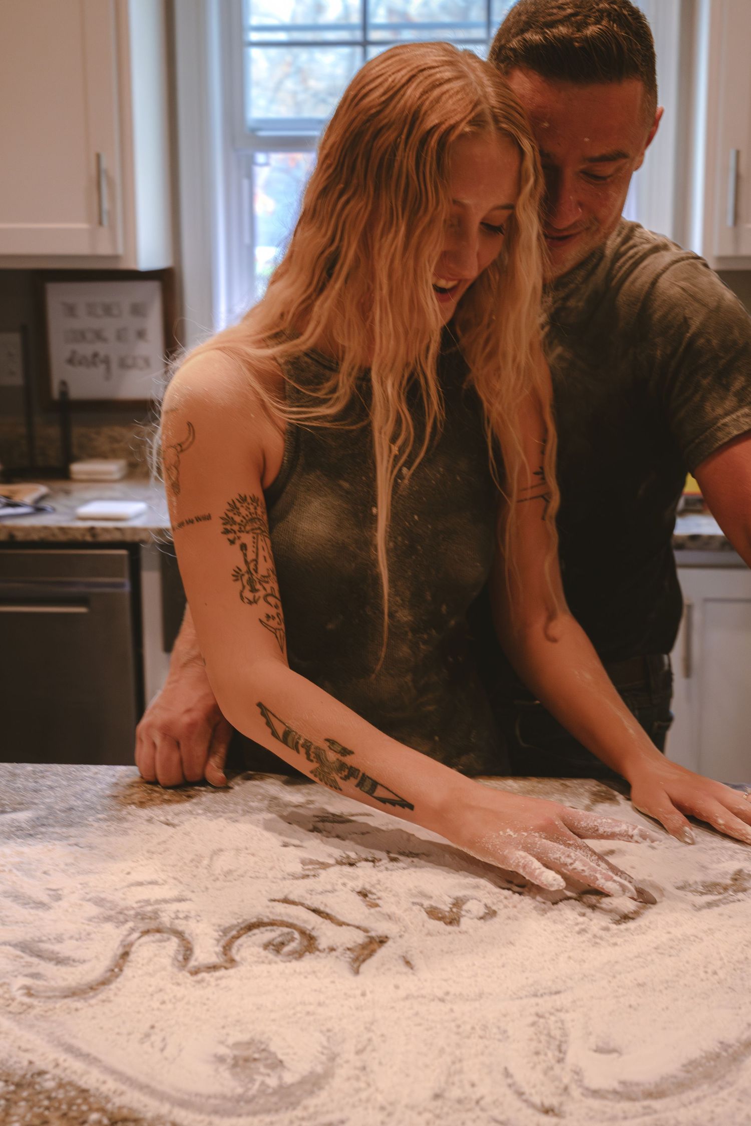 Couple drawing hearts in flour spread across a kitchen counter.