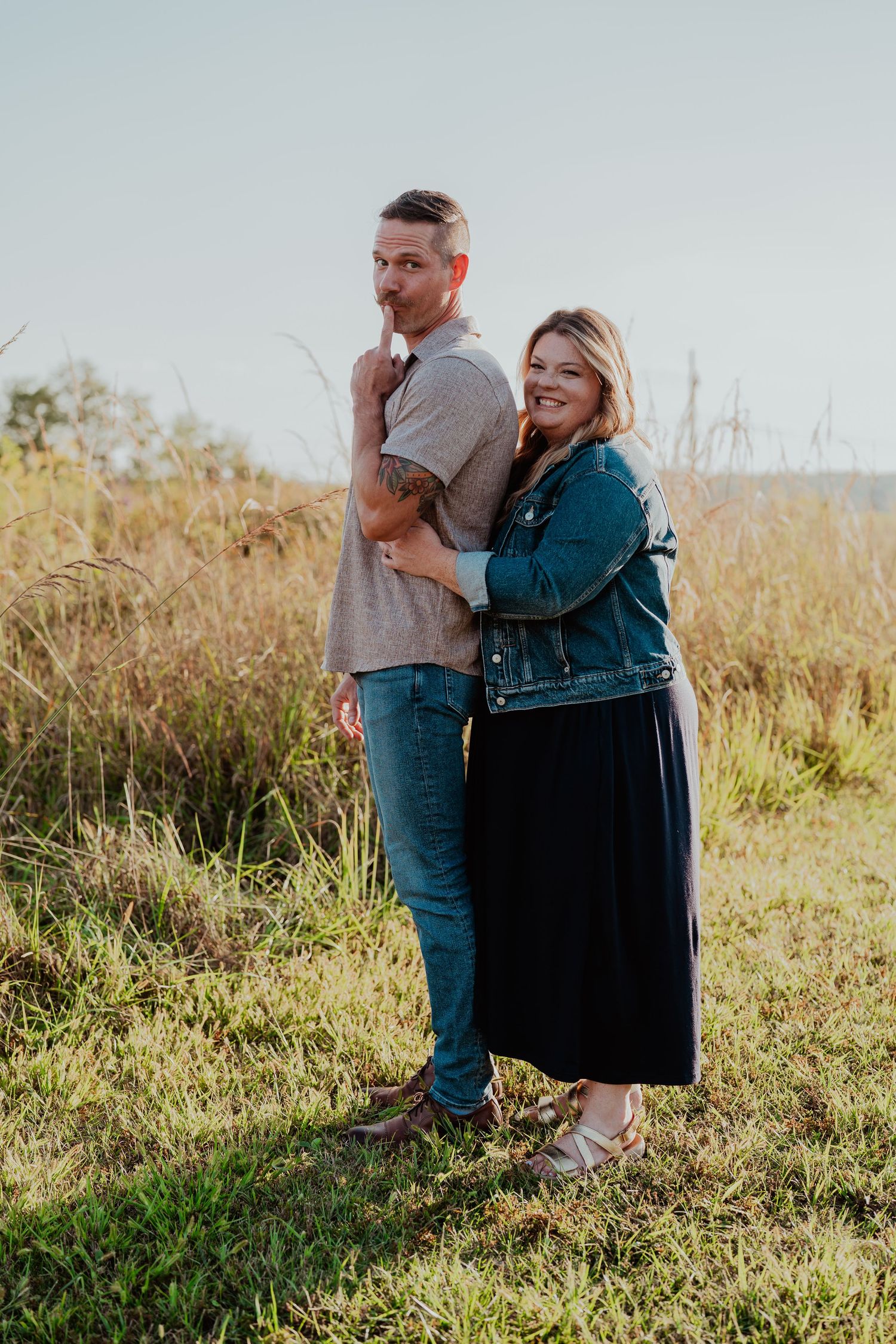 A couple embraces while sitting together on a grassy hillside during golden hour.