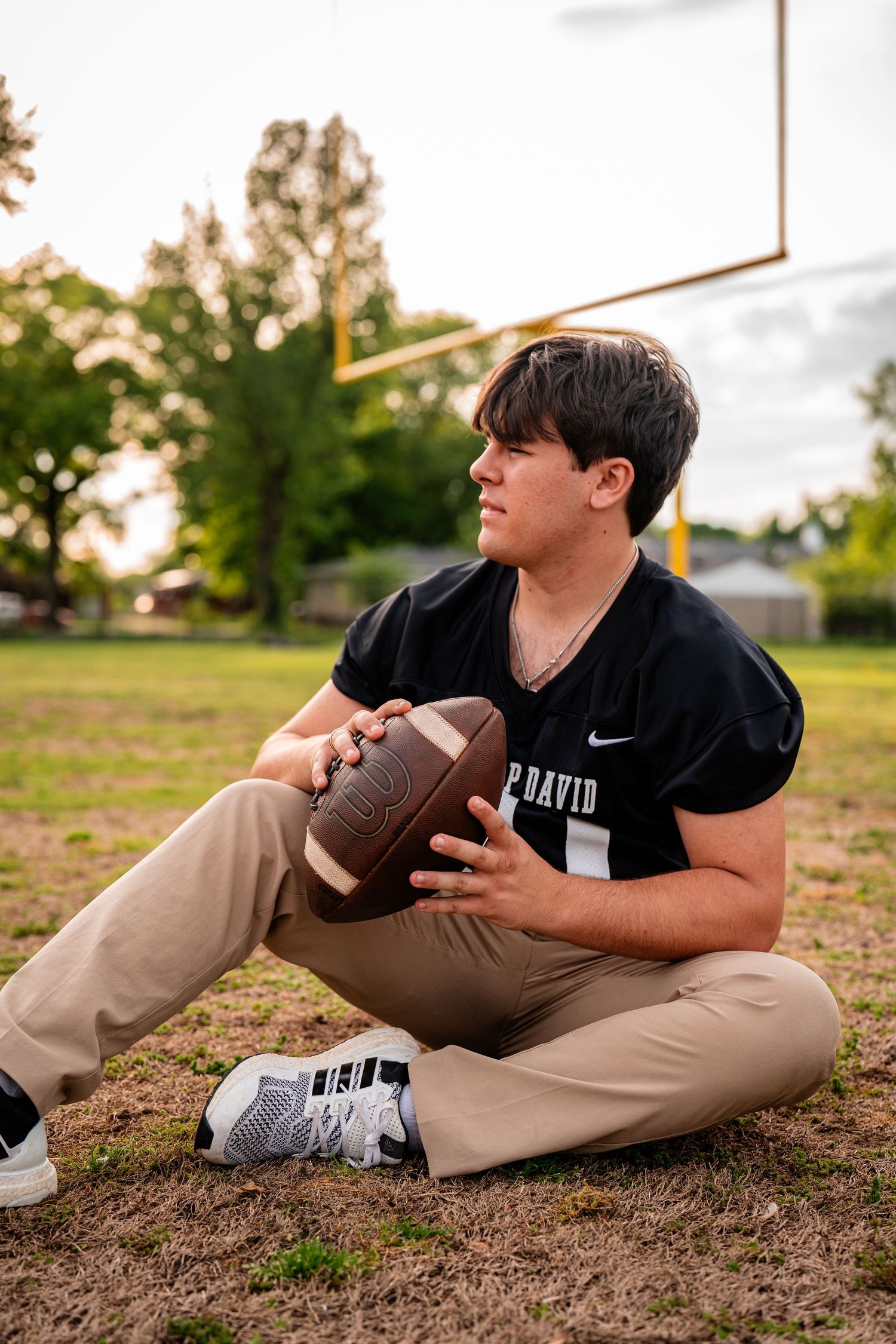 Athlete poses with football on grass field during sunset photoshoot.
