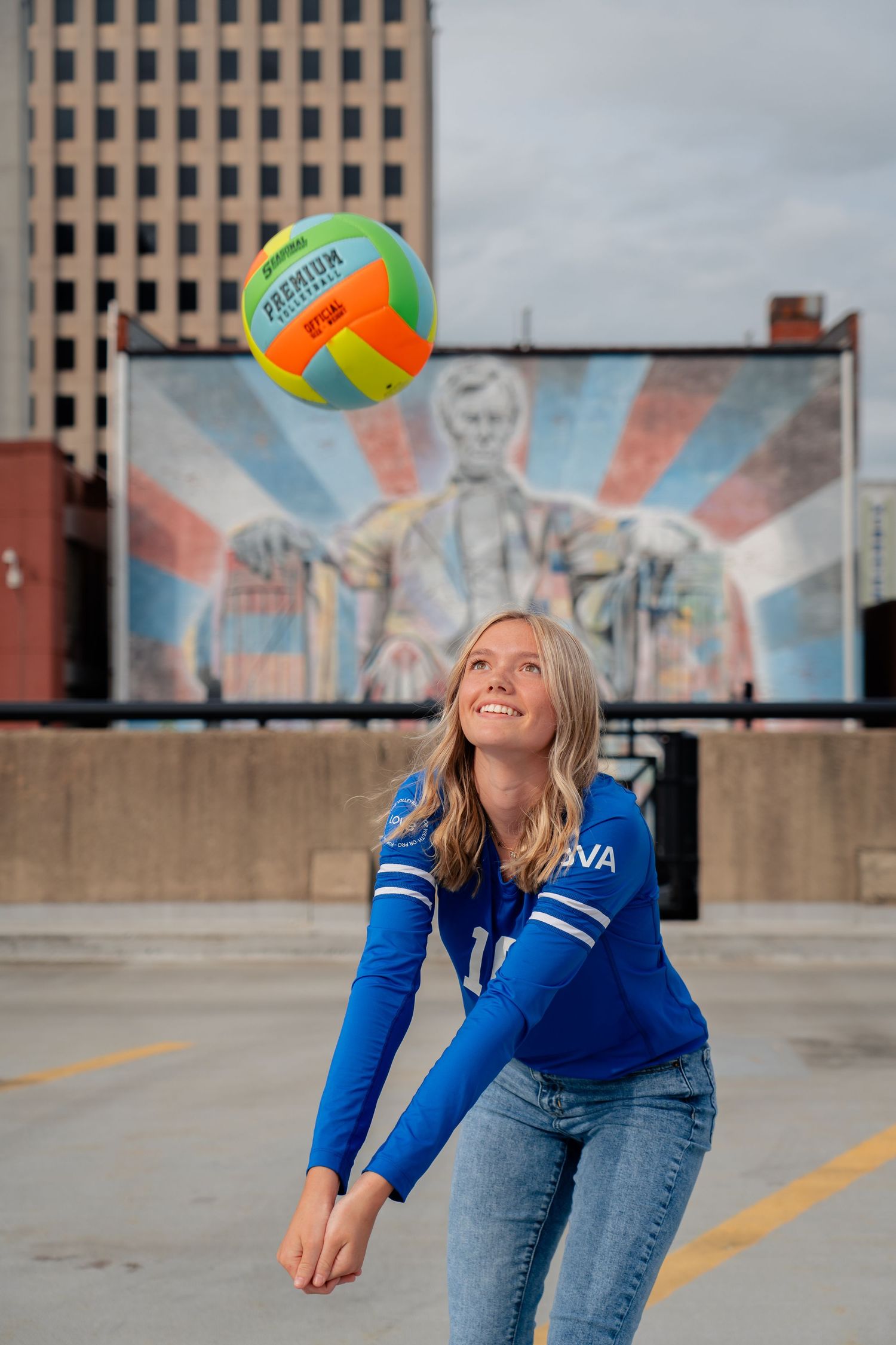 Person in blue jersey playing volleyball in urban setting with colorful mural background.