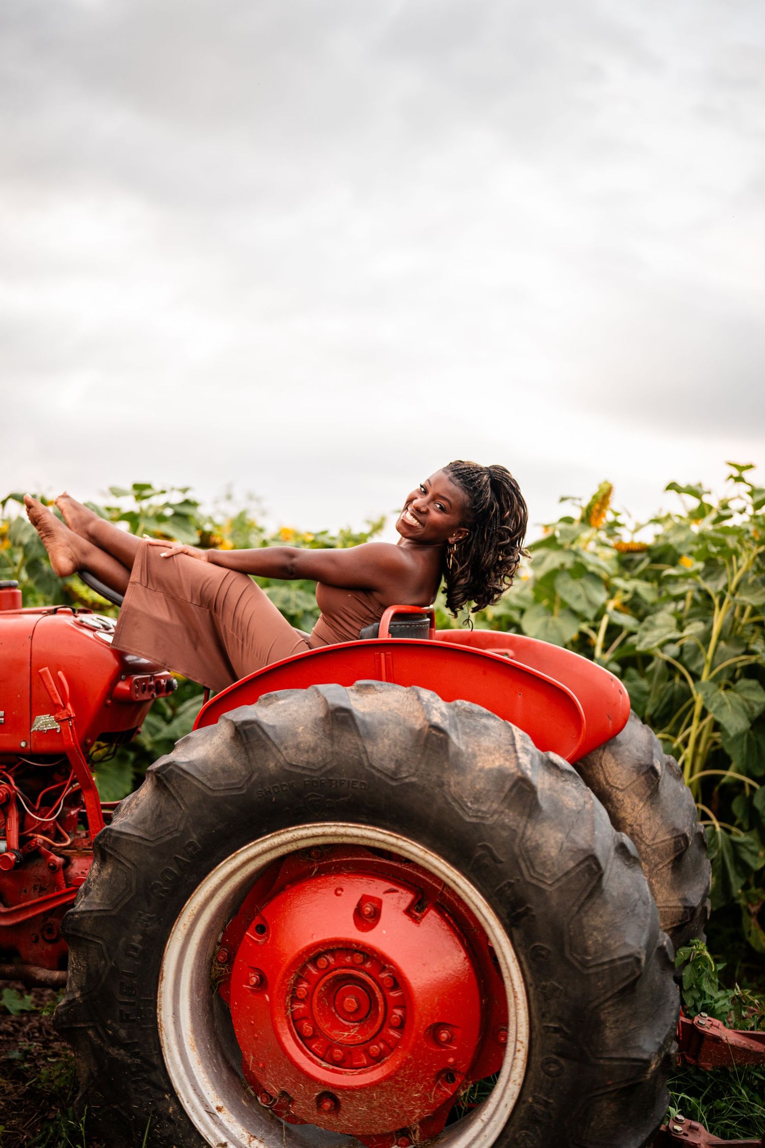 Person lounging on a vintage red tractor tire in a sunlit field.