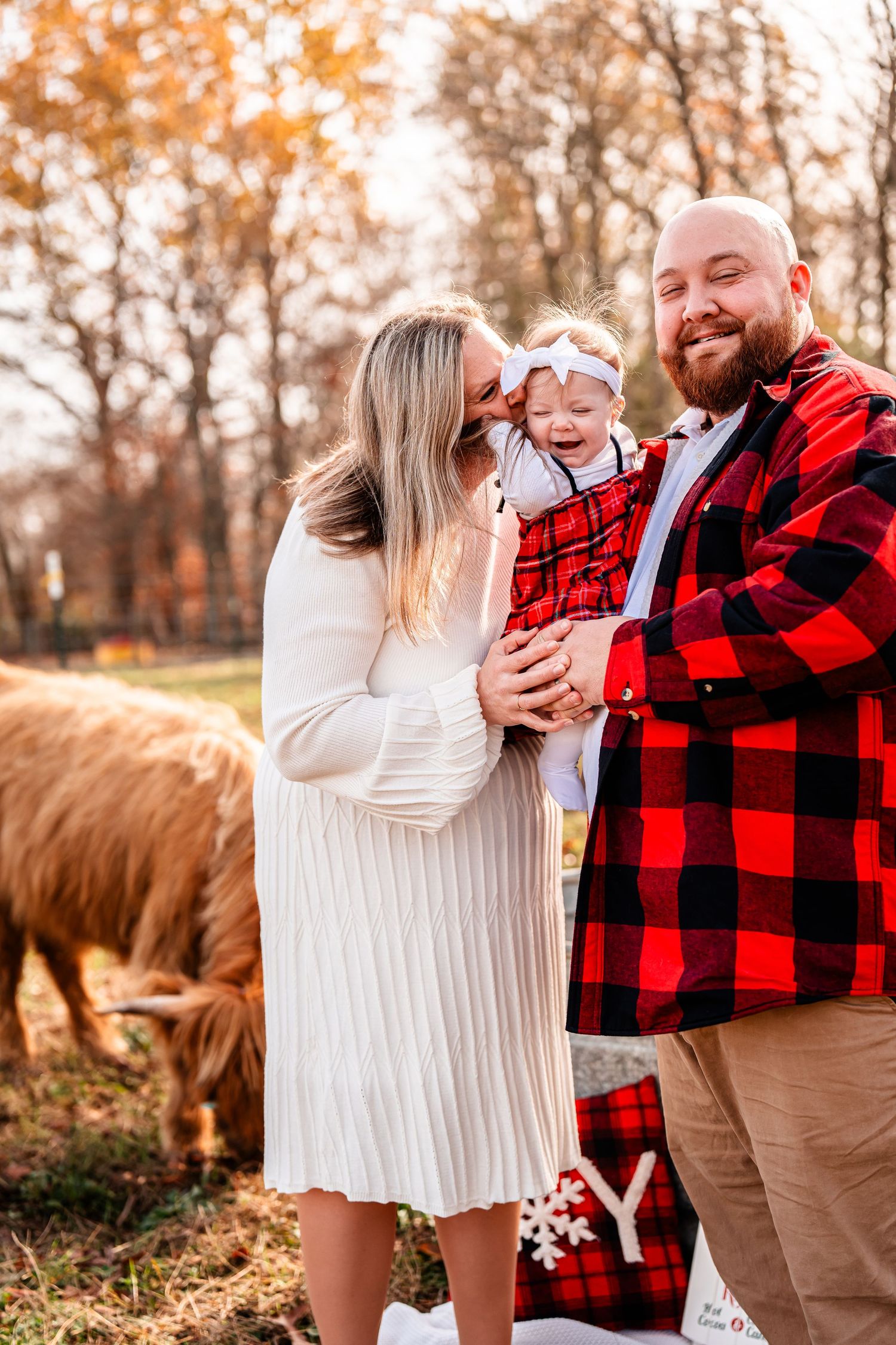 A family shares a joyful moment together outdoors with autumn trees and a horse in the background.