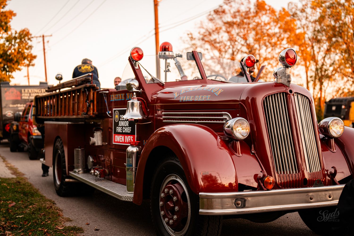 Vintage red fire trucks line up in a parade formation during golden hour.