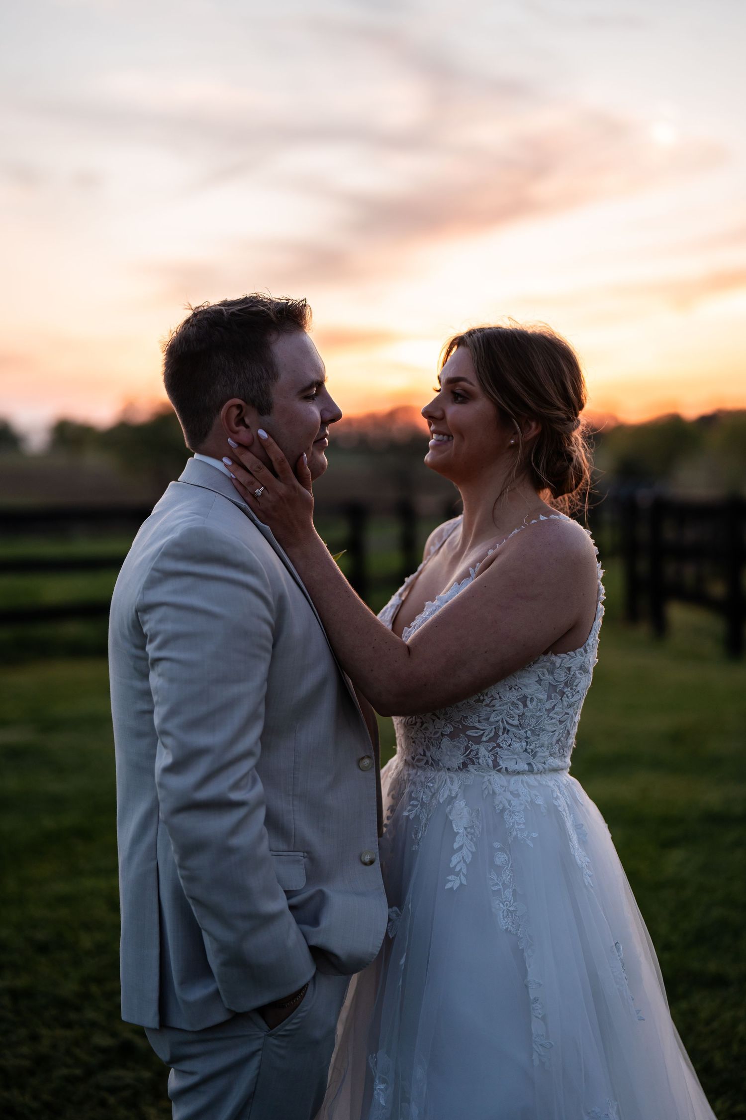 A romantic sunset moment between newlyweds in formal attire against a pastoral backdrop.