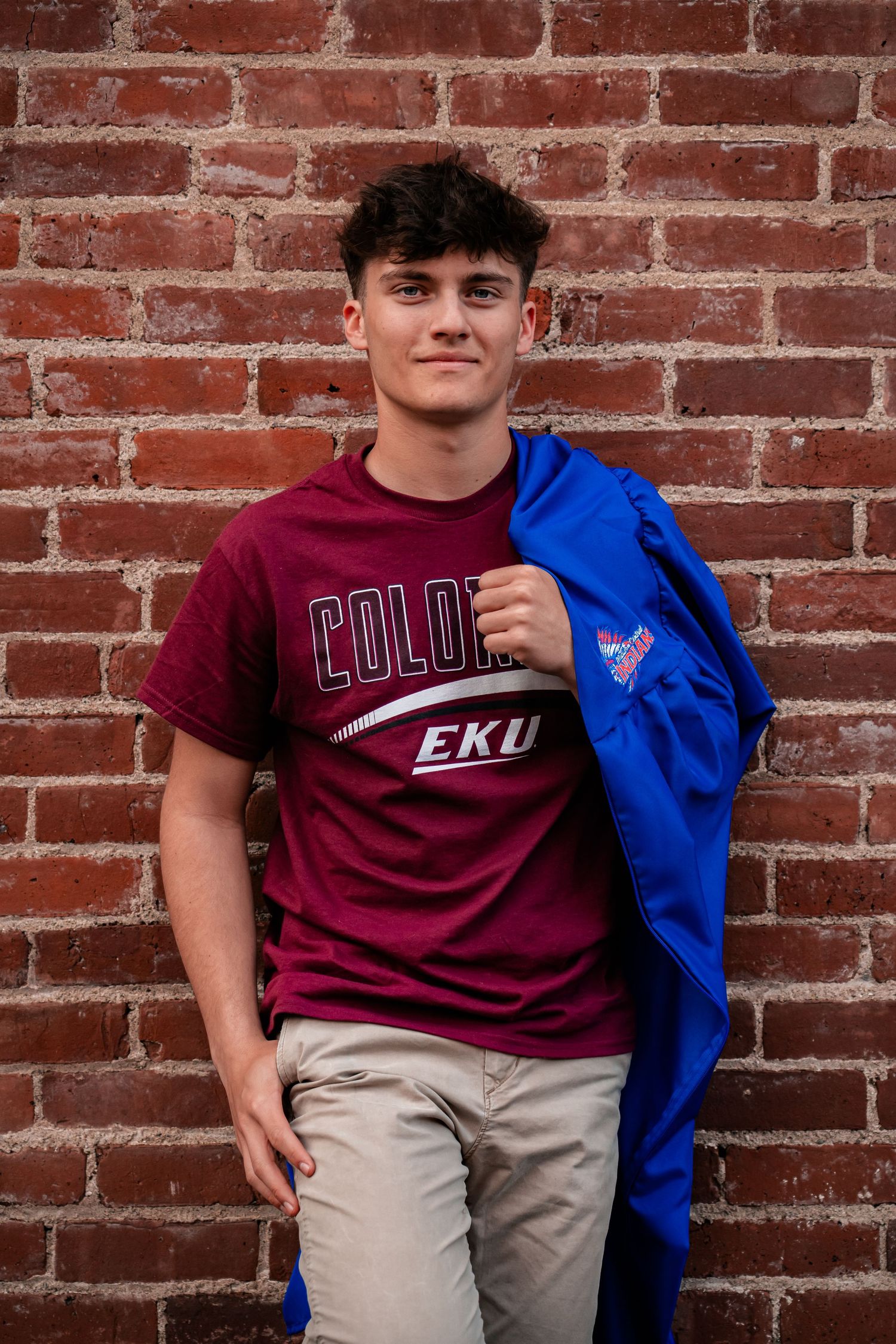 Student wearing maroon college apparel poses against rustic brick wall backdrop.