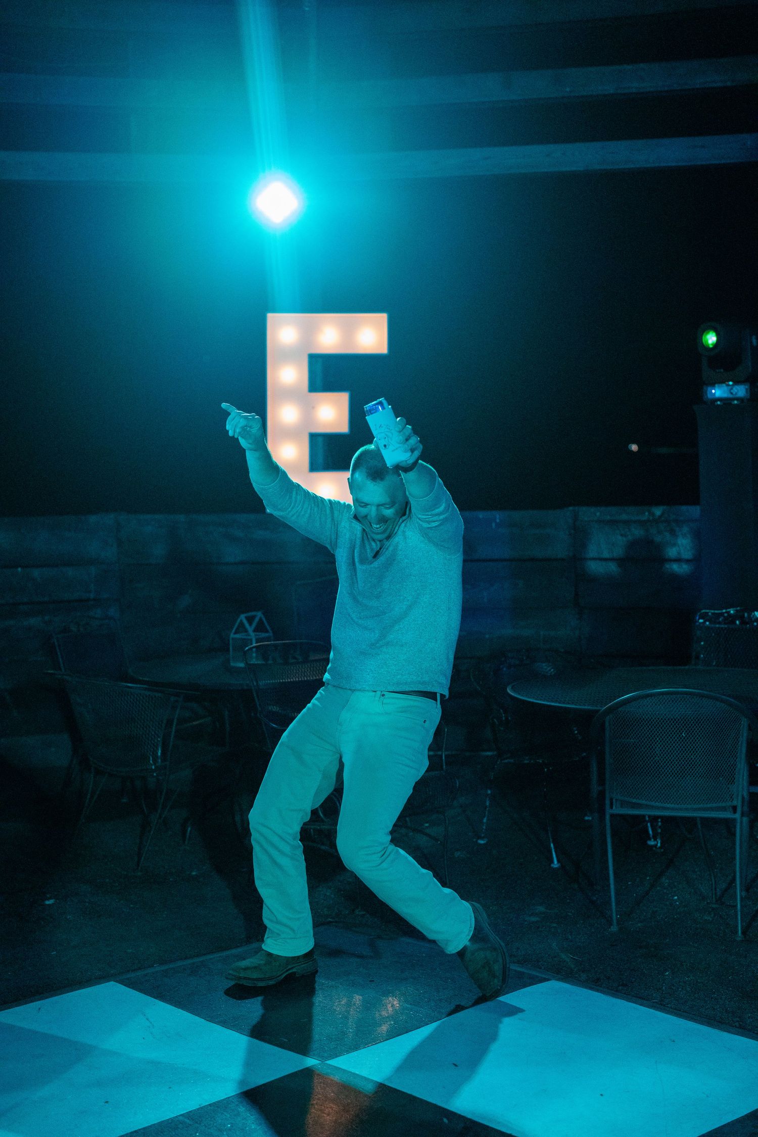 Silhouette of person dancing under blue lighting on checkered dance floor.