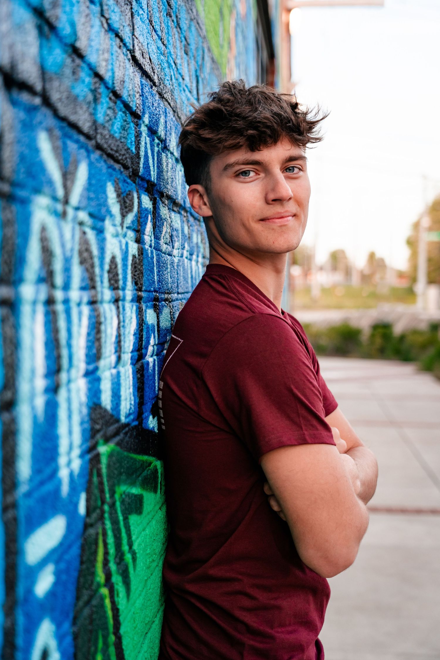Casual portrait against colorful street art wall with blue and green graffiti designs.