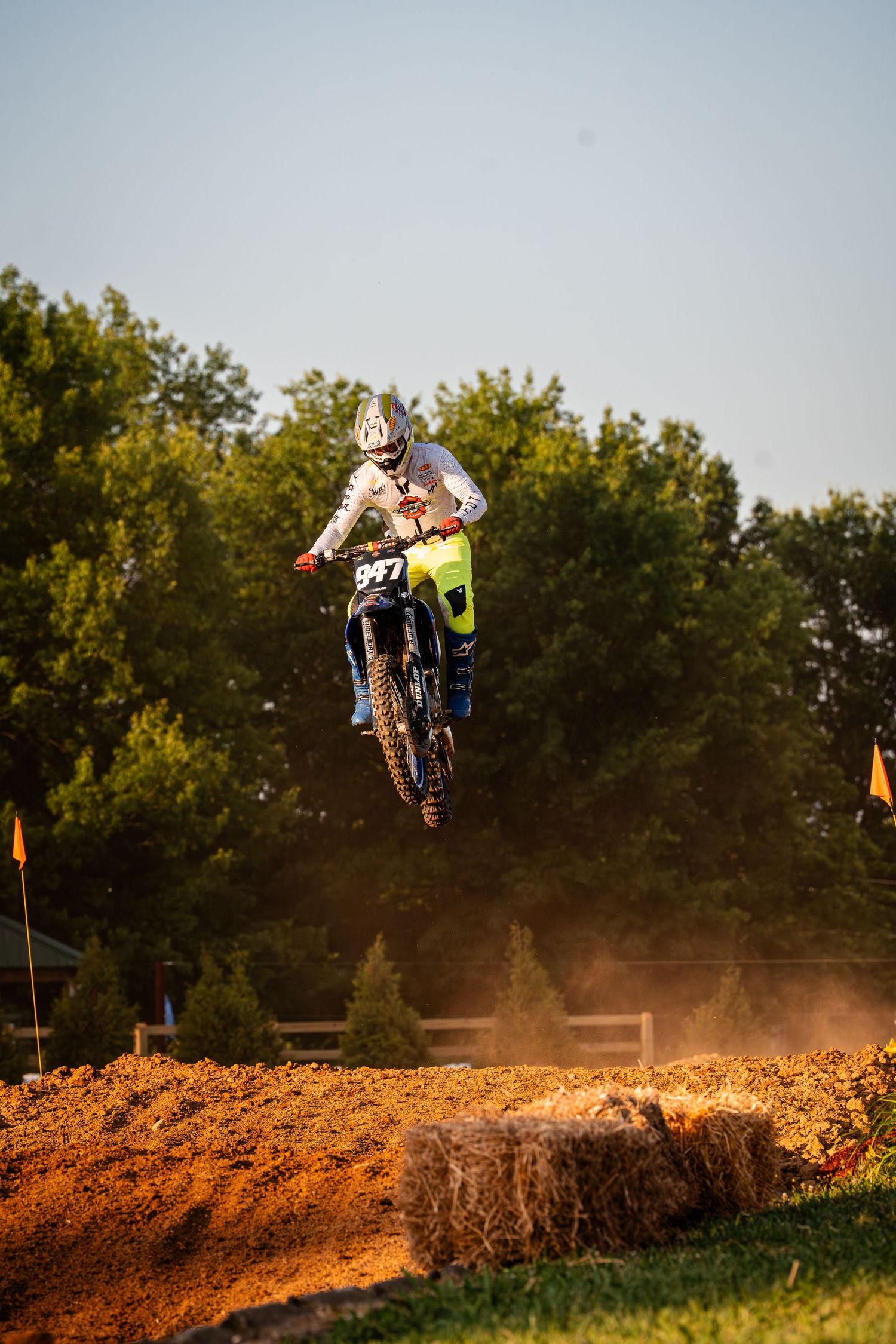 Motorcycle rider catches air during sunset motocross jump on dirt track.