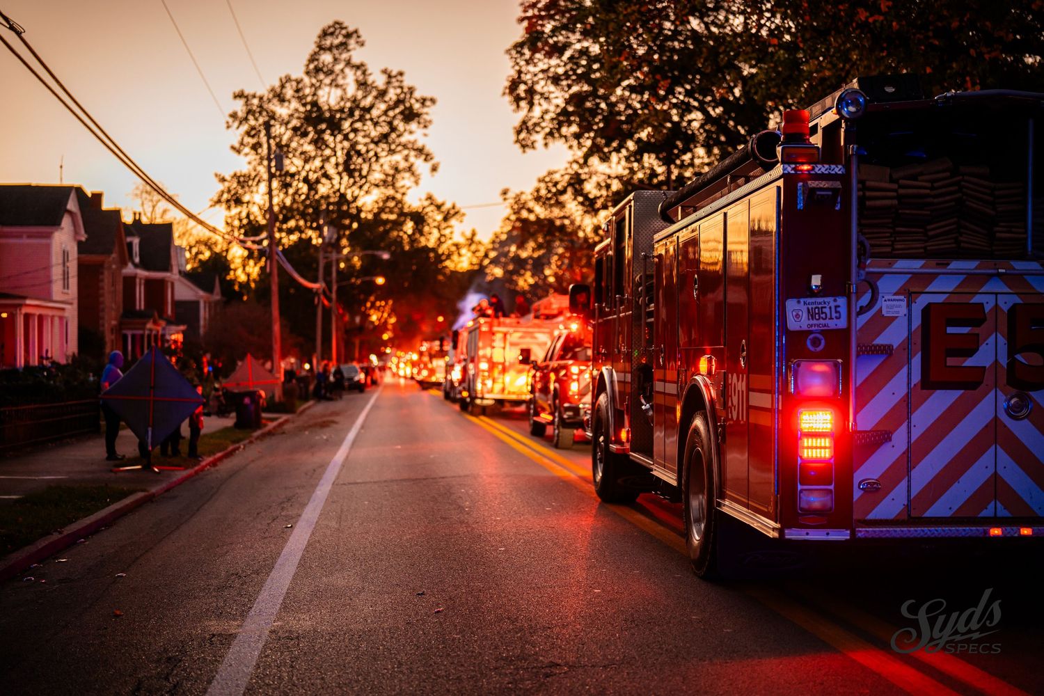 Emergency vehicles with flashing lights illuminate a darkened street at dusk.