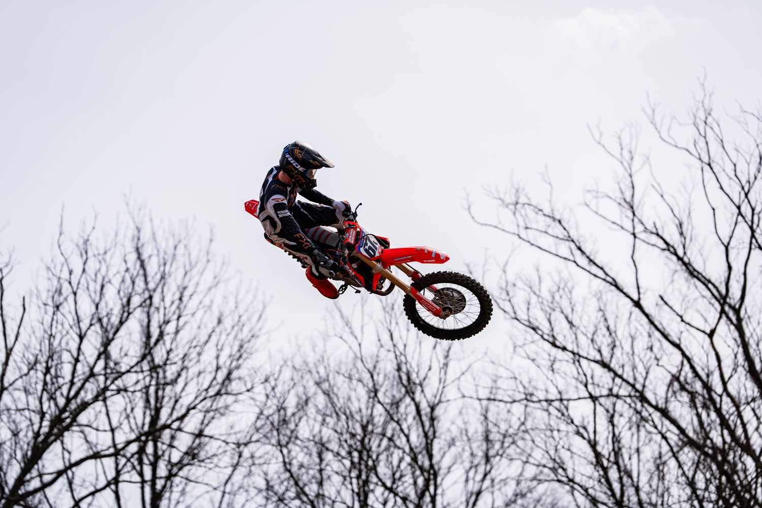 A person on a red motorcycle performing a jump over a barren, wintry landscape.