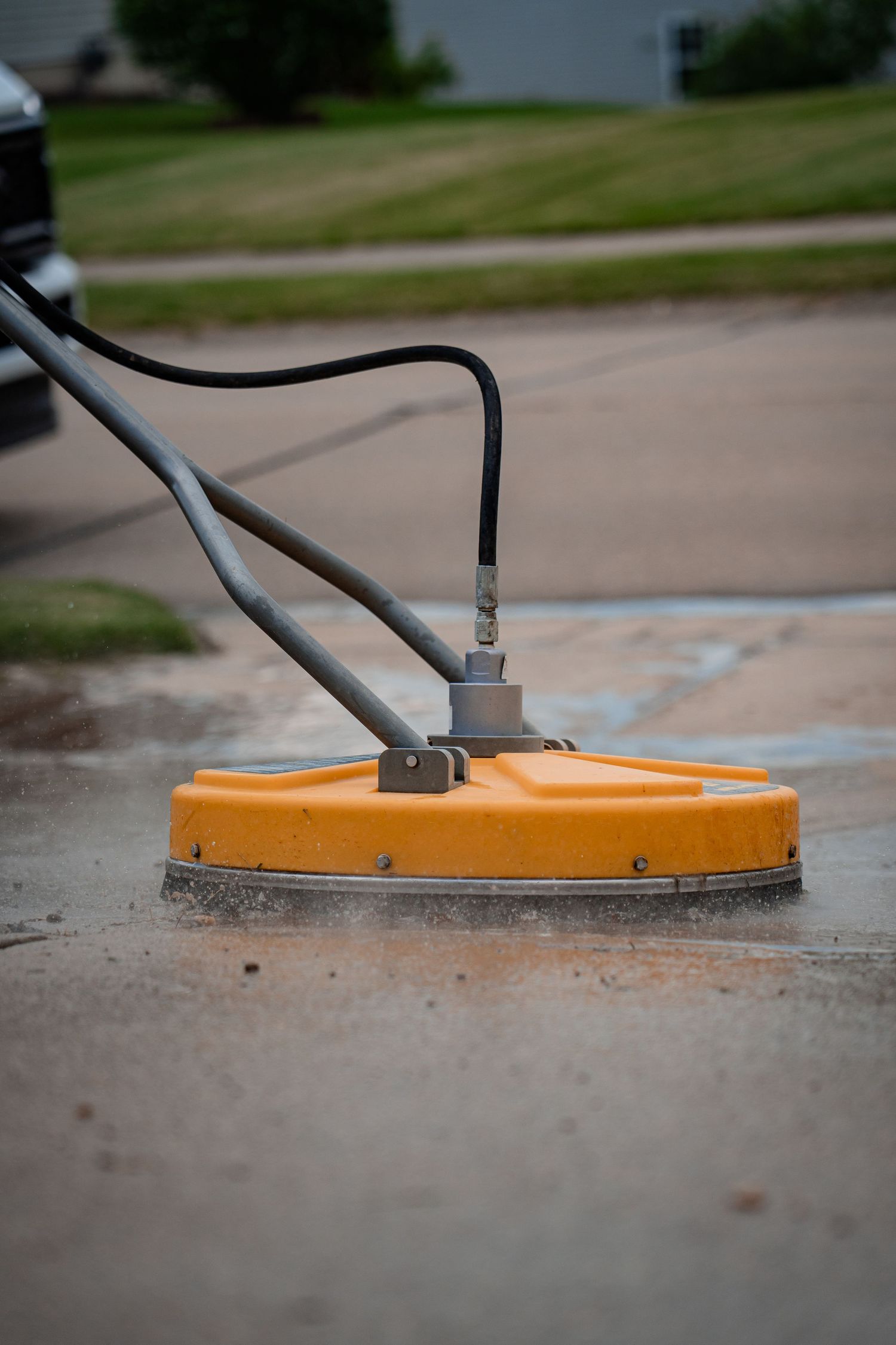 Close-up sequence showing an orange surface cleaner attachment for pressure washing concrete.