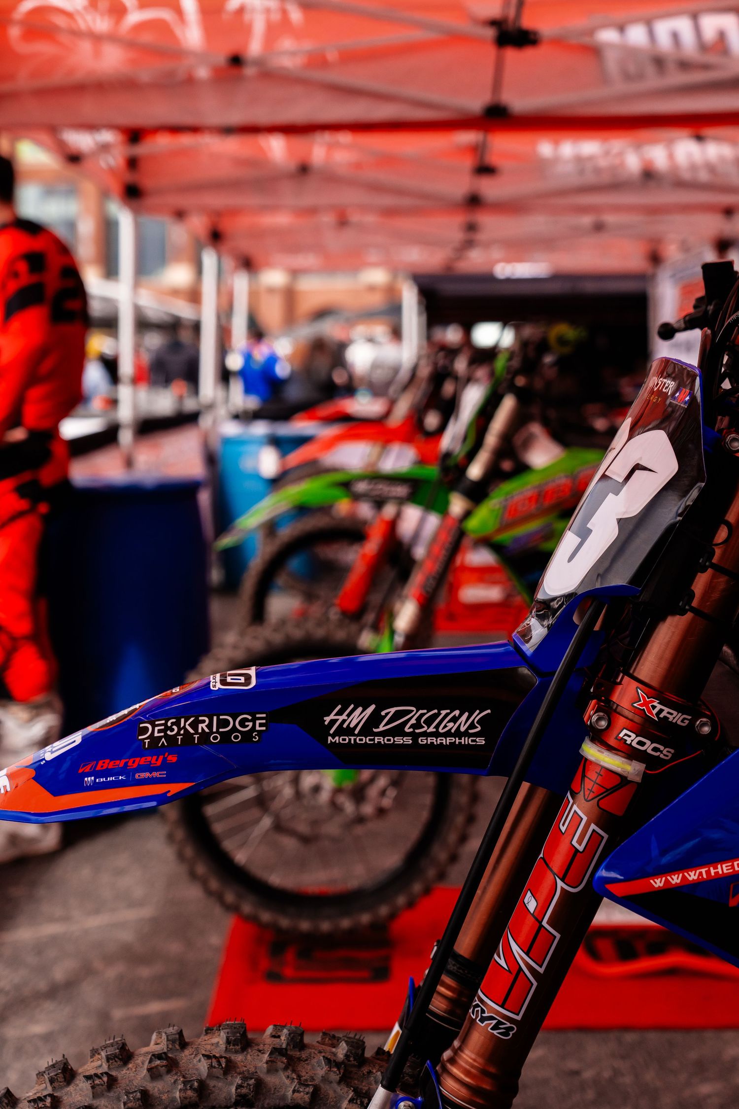 Blue and white racing dirt bike with sponsor decals displayed at an outdoor event.