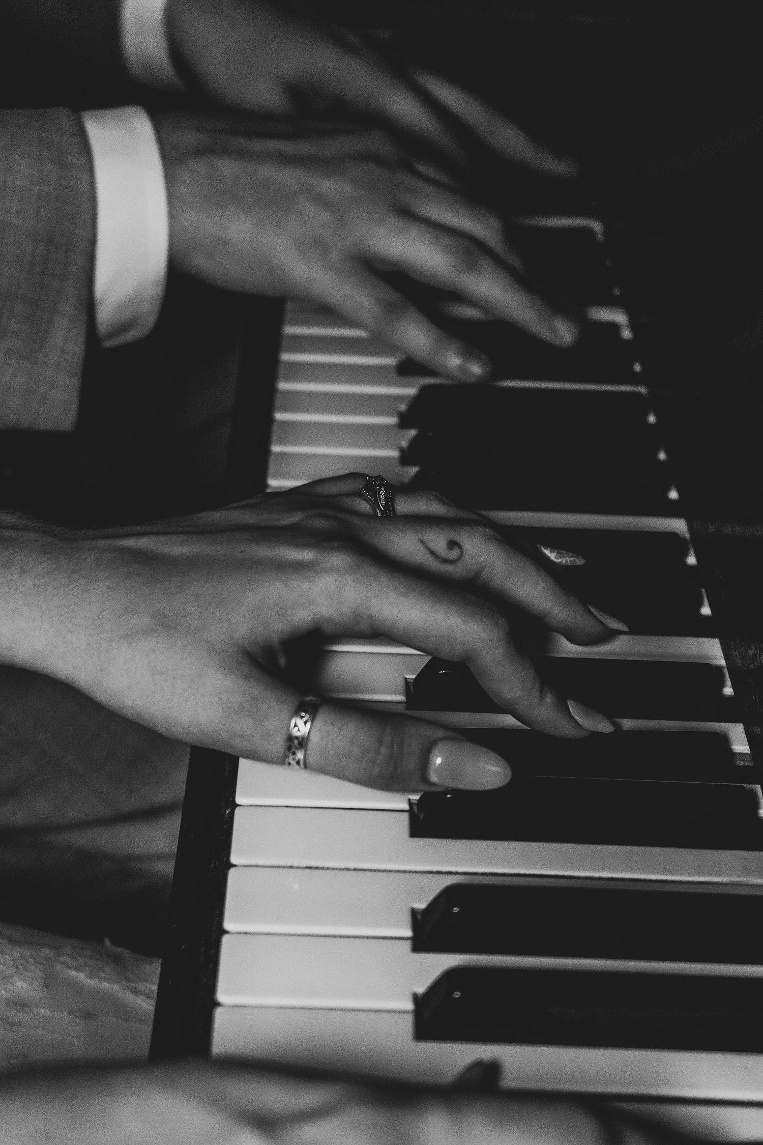 Close-up black and white photo of hands playing piano keys with ring visible.