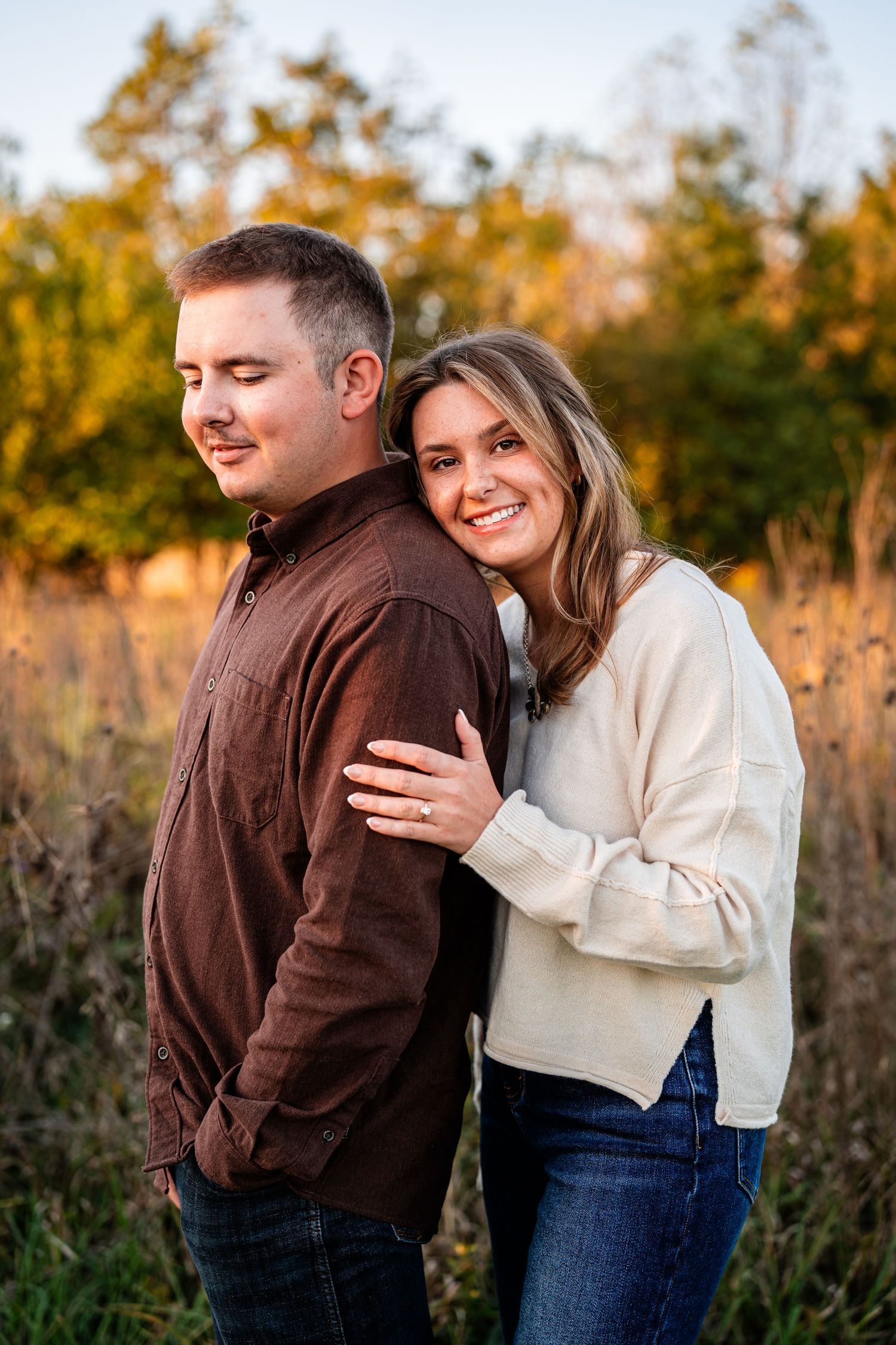 Romantic autumn engagement photos of couple in brown jacket and cream sweater outdoors at sunset.