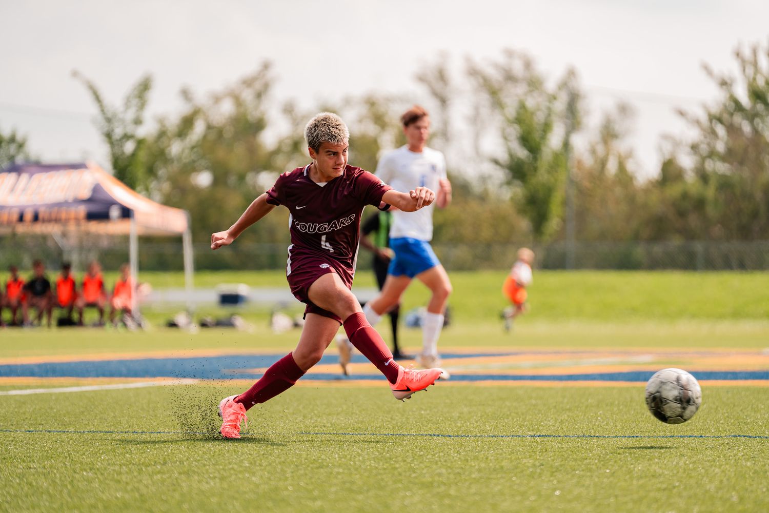 Soccer player in maroon uniform prepares to kick ball during outdoor match.