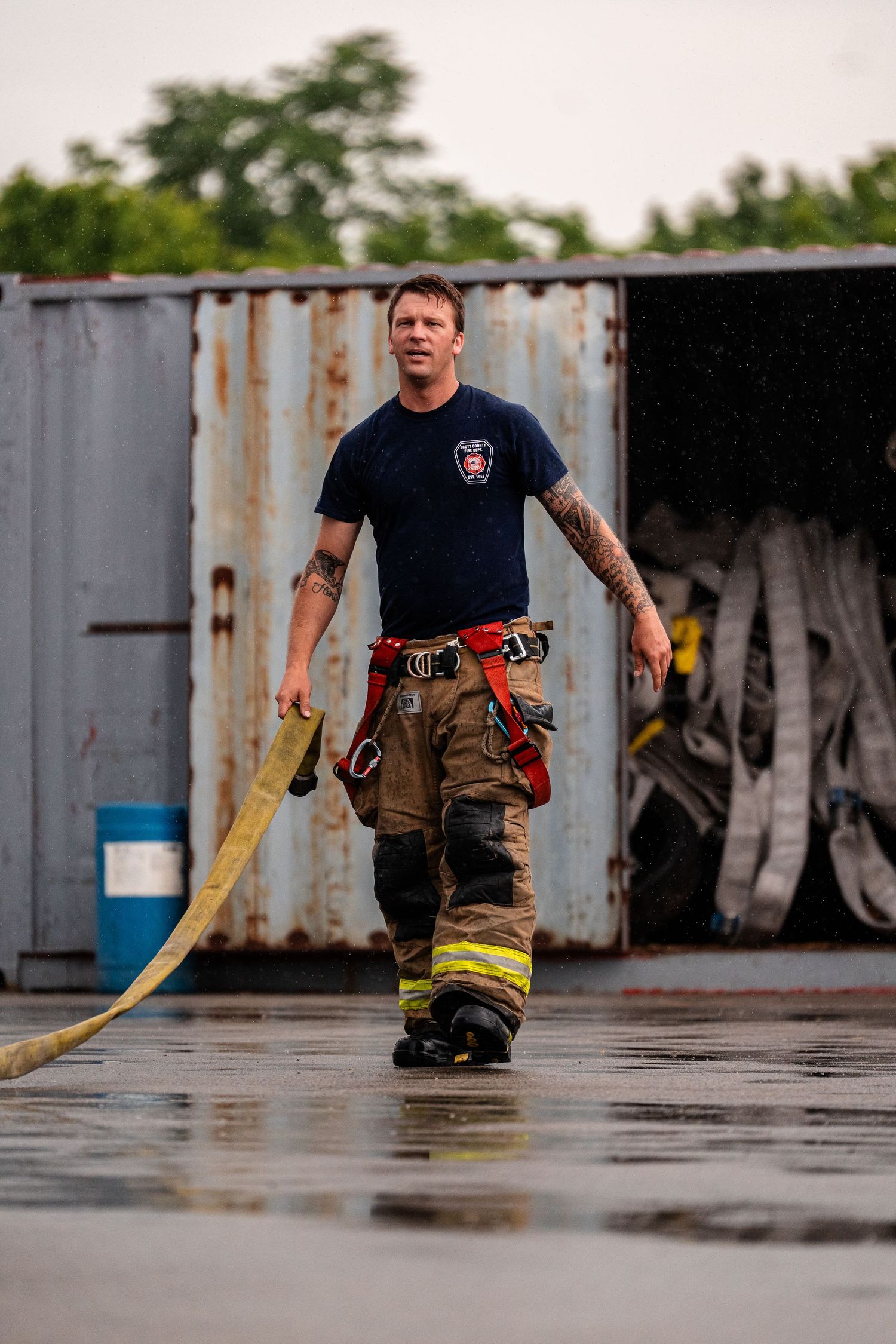 Firefighters in uniform practice hose handling techniques on a wet training ground.