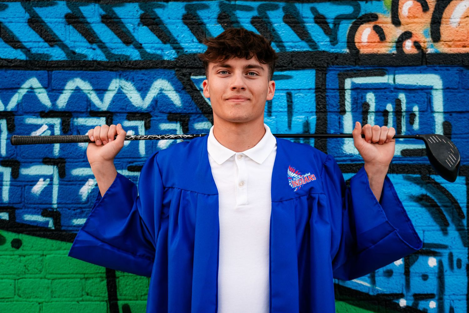 Group photo against blue graffiti wall wearing matching blue graduation gowns.