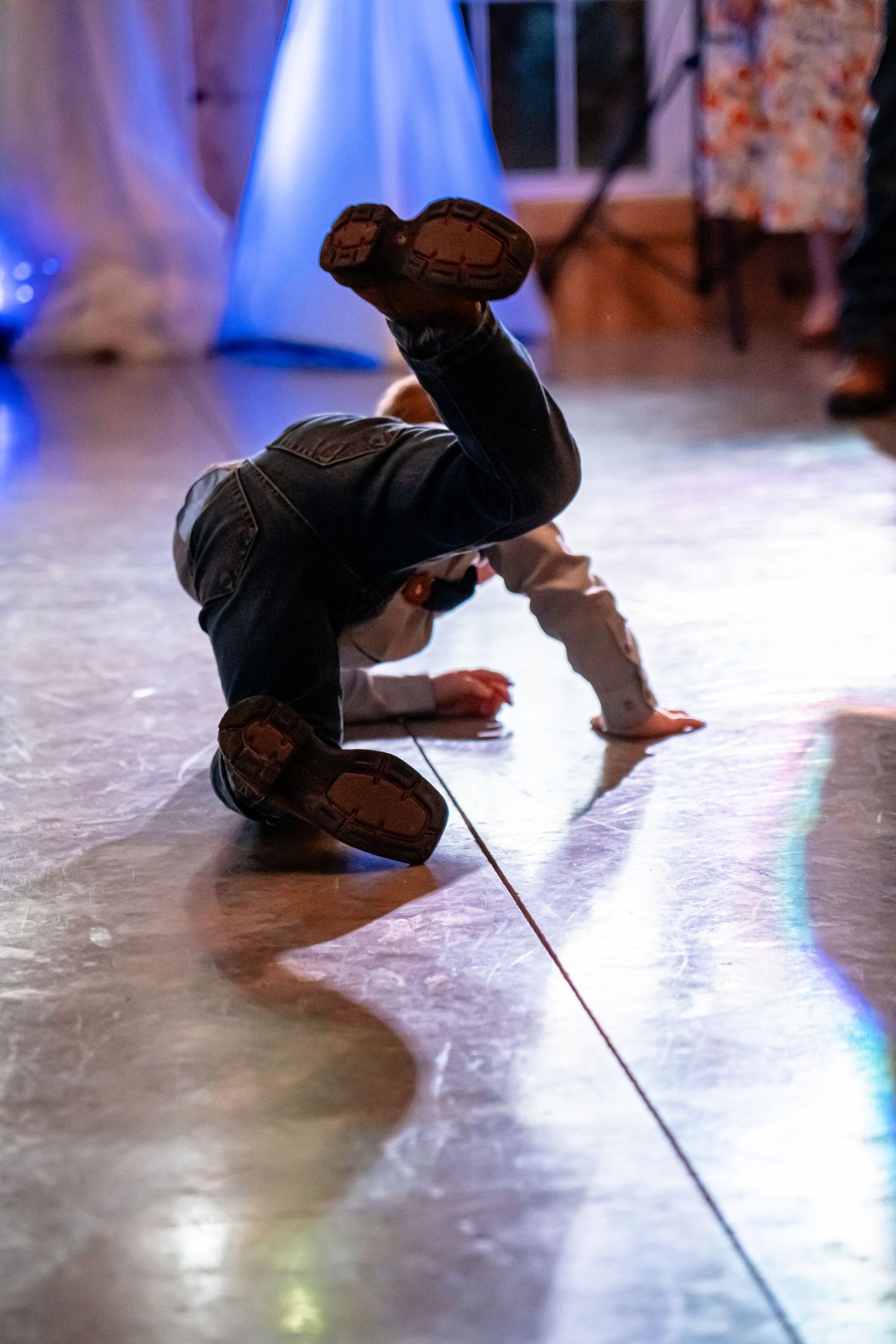 Dancer performs breakdancing move on illuminated dance floor at reception.