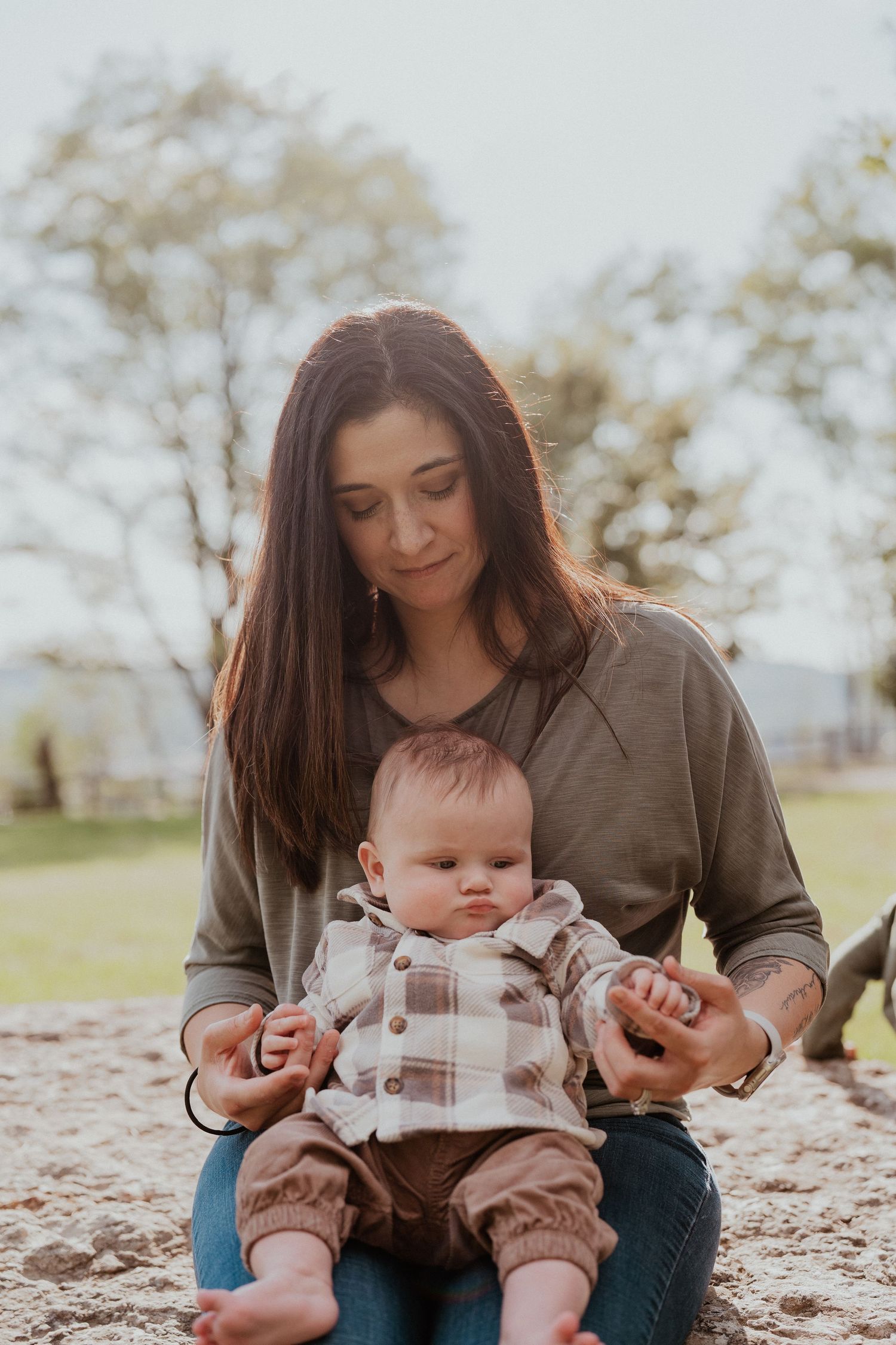 Parent and baby sharing a tender moment while sitting on a blanket outdoors.