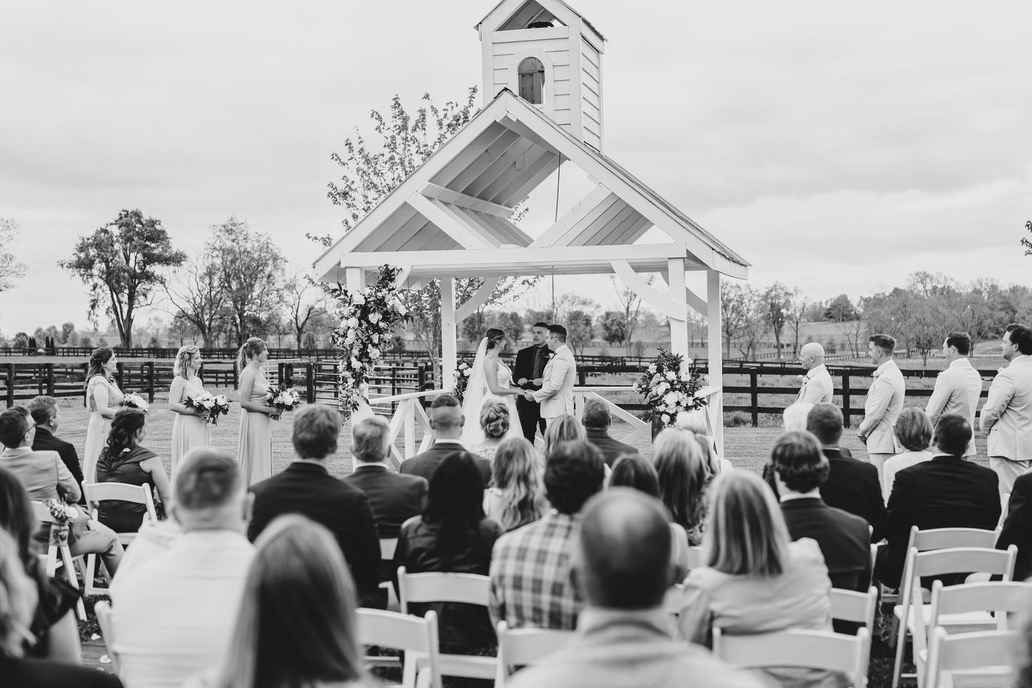 Panoramic view of outdoor wedding ceremony with white chapel and seated guests.