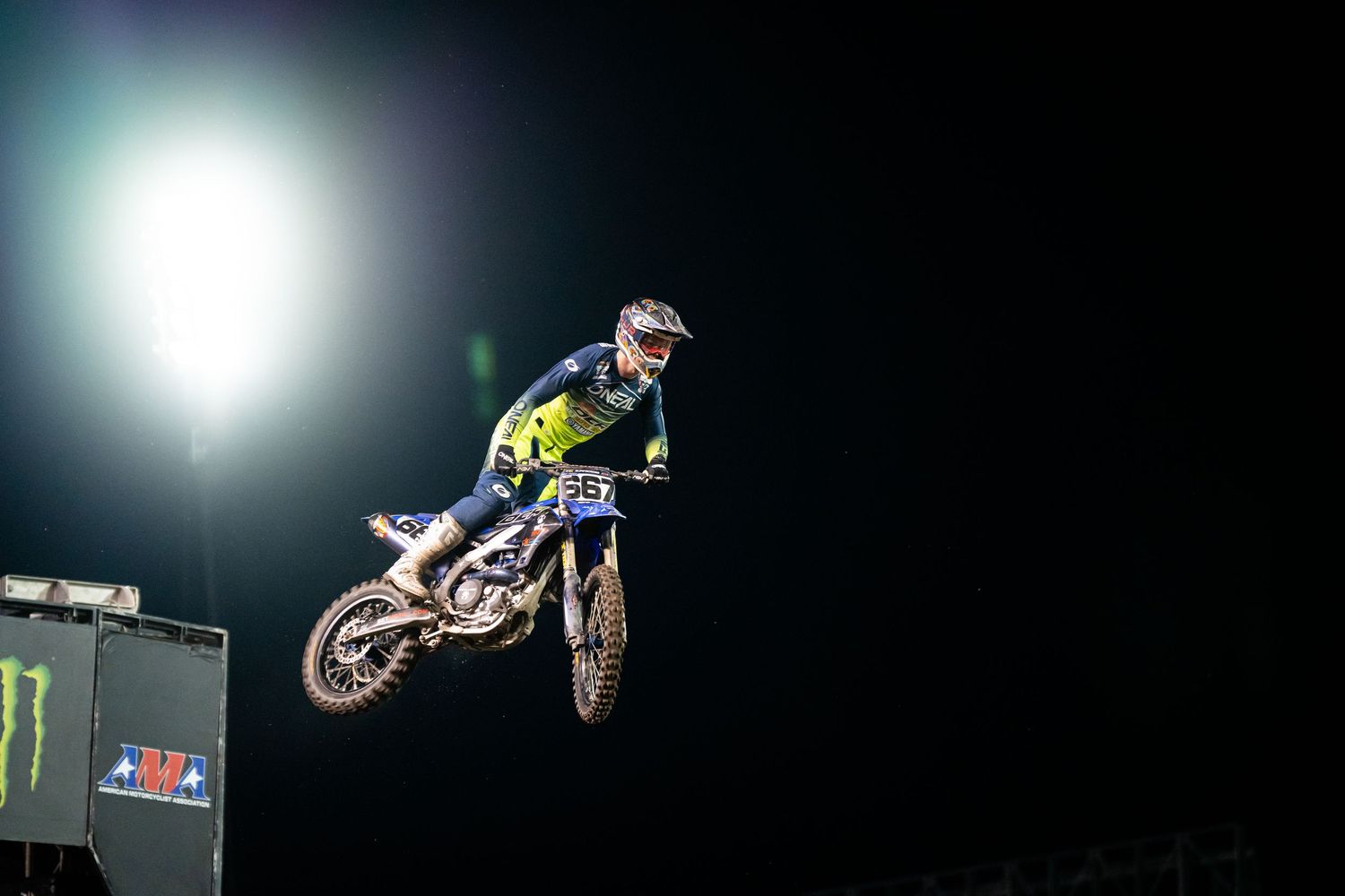 Motocross rider performing aerial stunt against night sky with stadium lights.