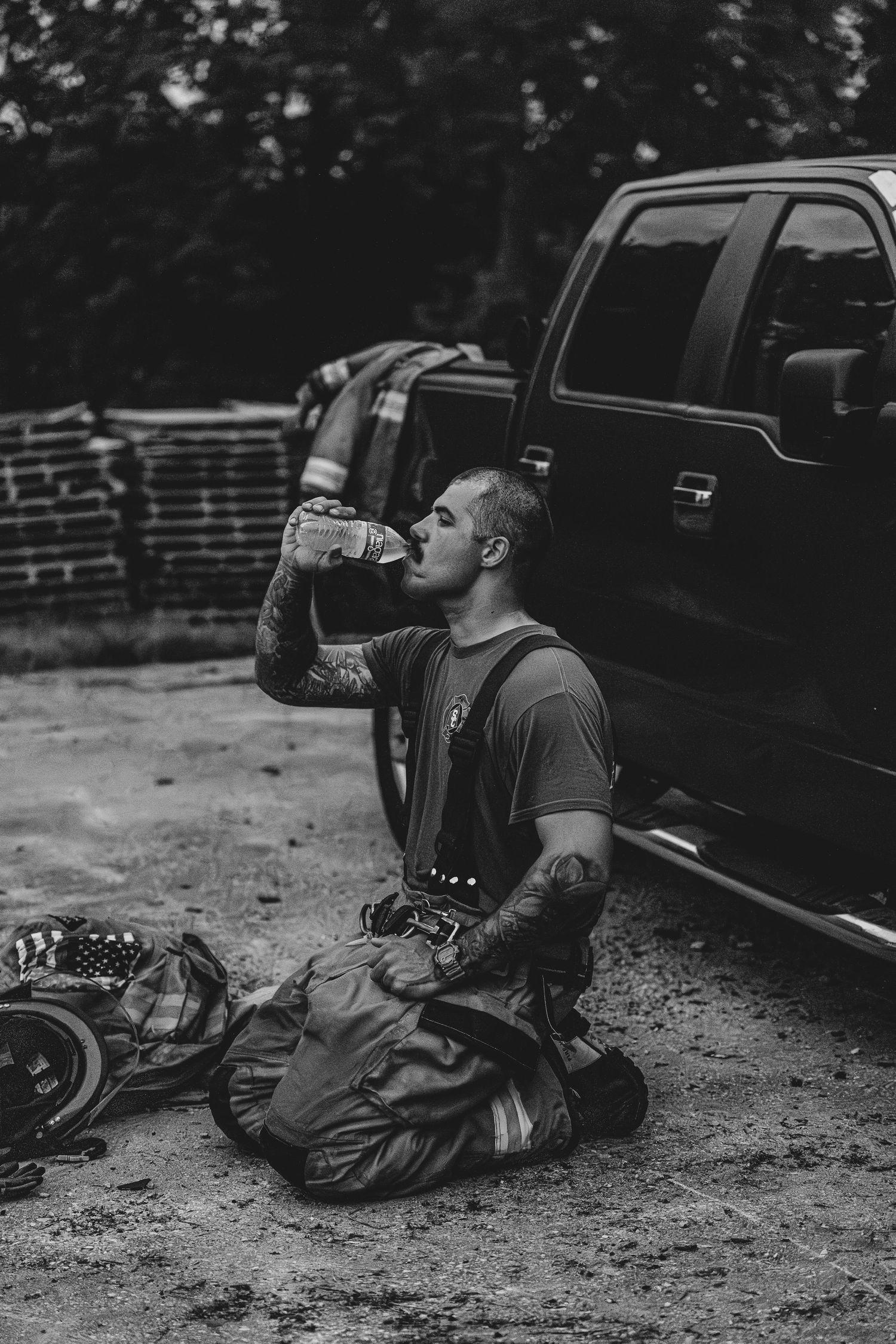 A person in work gear takes a drink while sitting next to a black pickup truck.