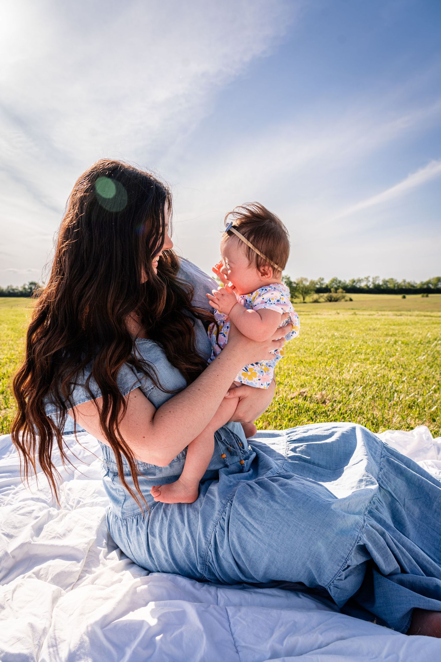 A peaceful moment on a blanket in a sunny meadow with gentle interaction and blue sky above.